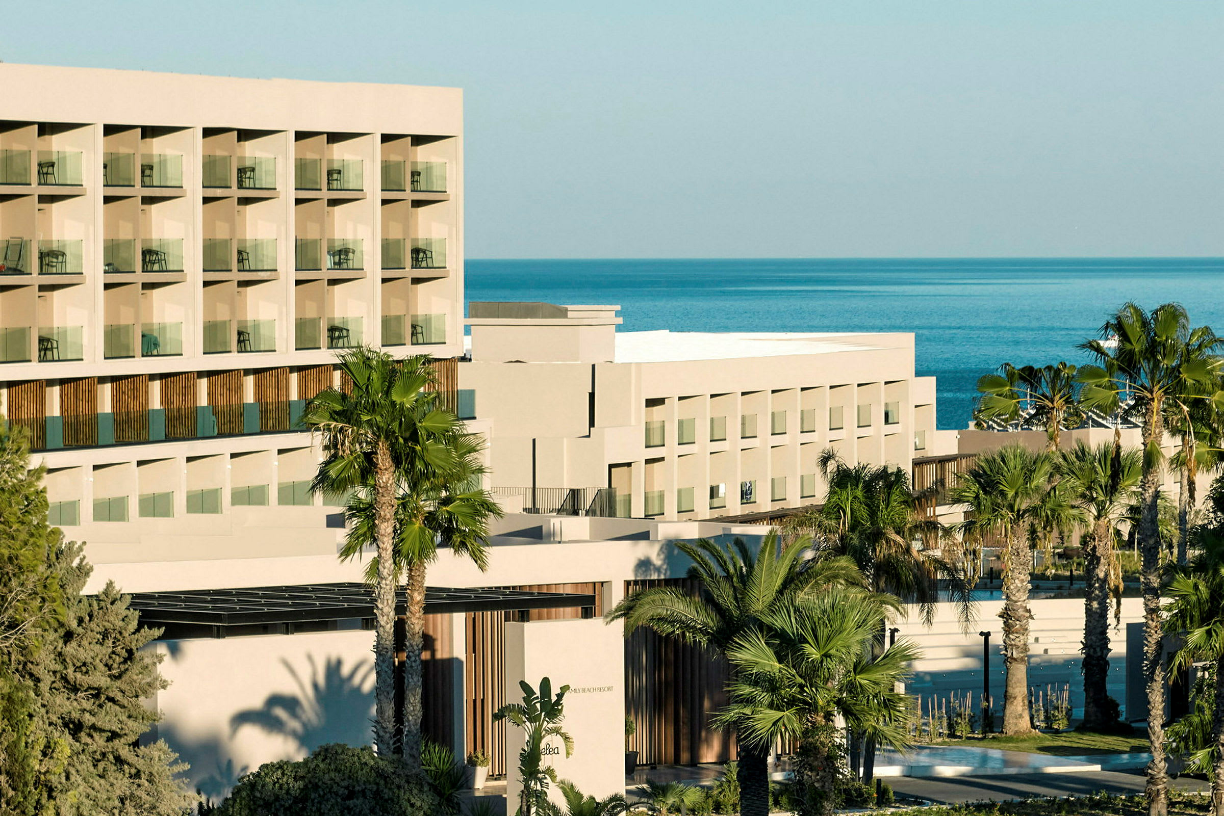 Bild av en modern hotellbyggnad med flera våningar och balkonger, omgiven av palmträd och med utsikt över havet. (AI-genererad text)