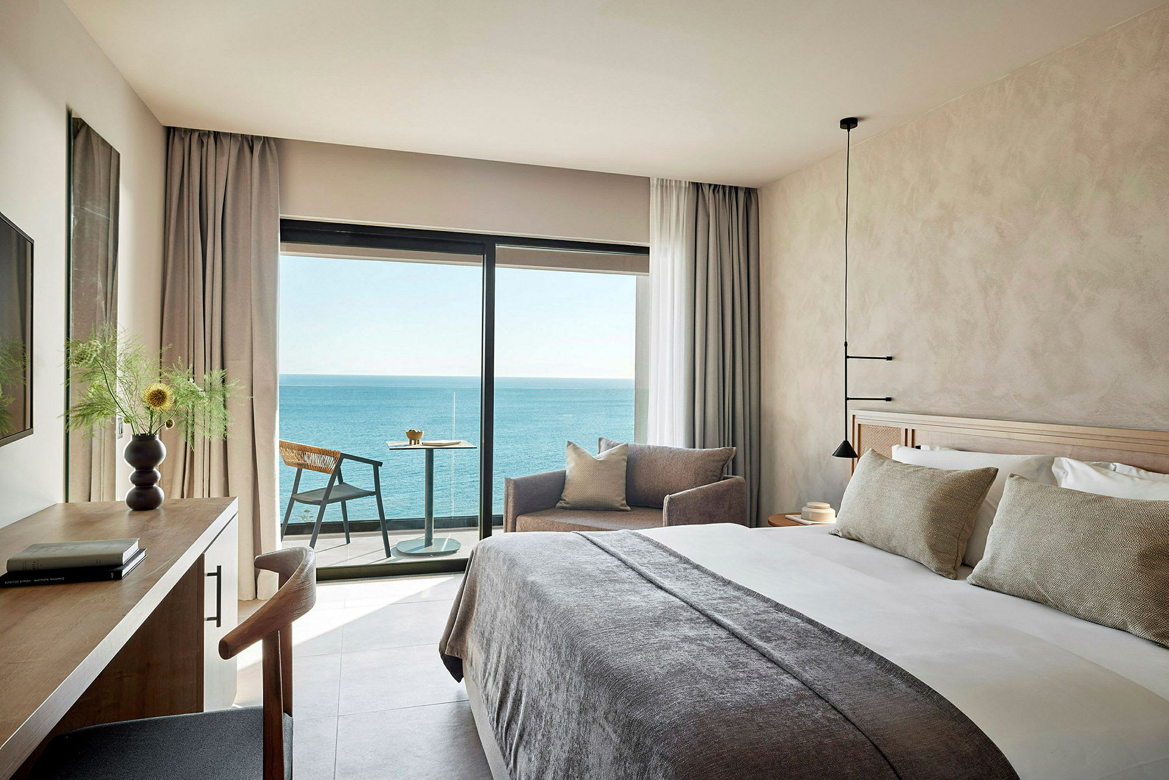 Ett modernt hotellrum med en stor säng, soffdel och skrivbord, samt en balkong med utsikt över havet. (AI-genererad text)