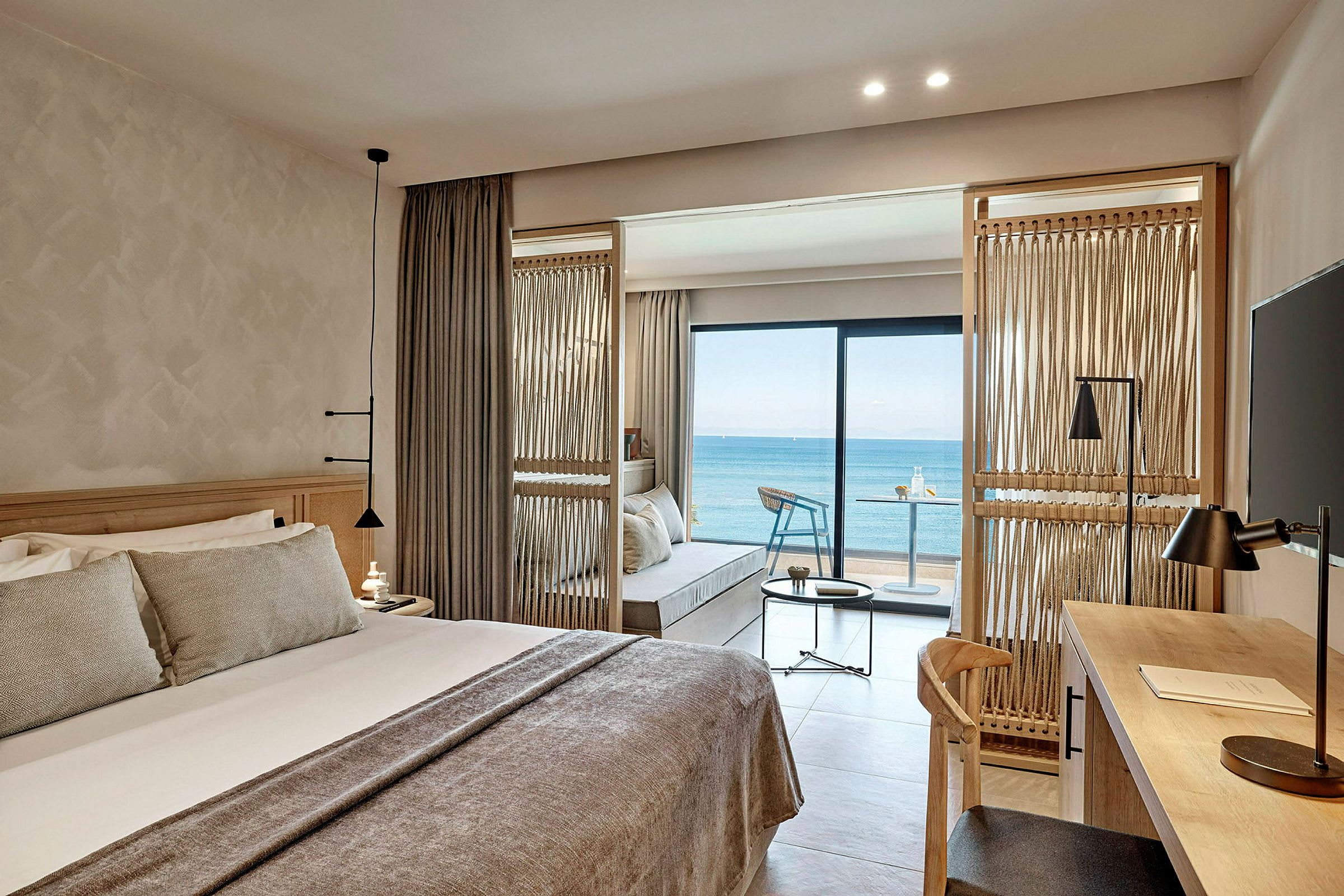 Bild av ett hotellrum med en säng, skrivbord och utsikt över havet från balkongen. (AI-genererad text)