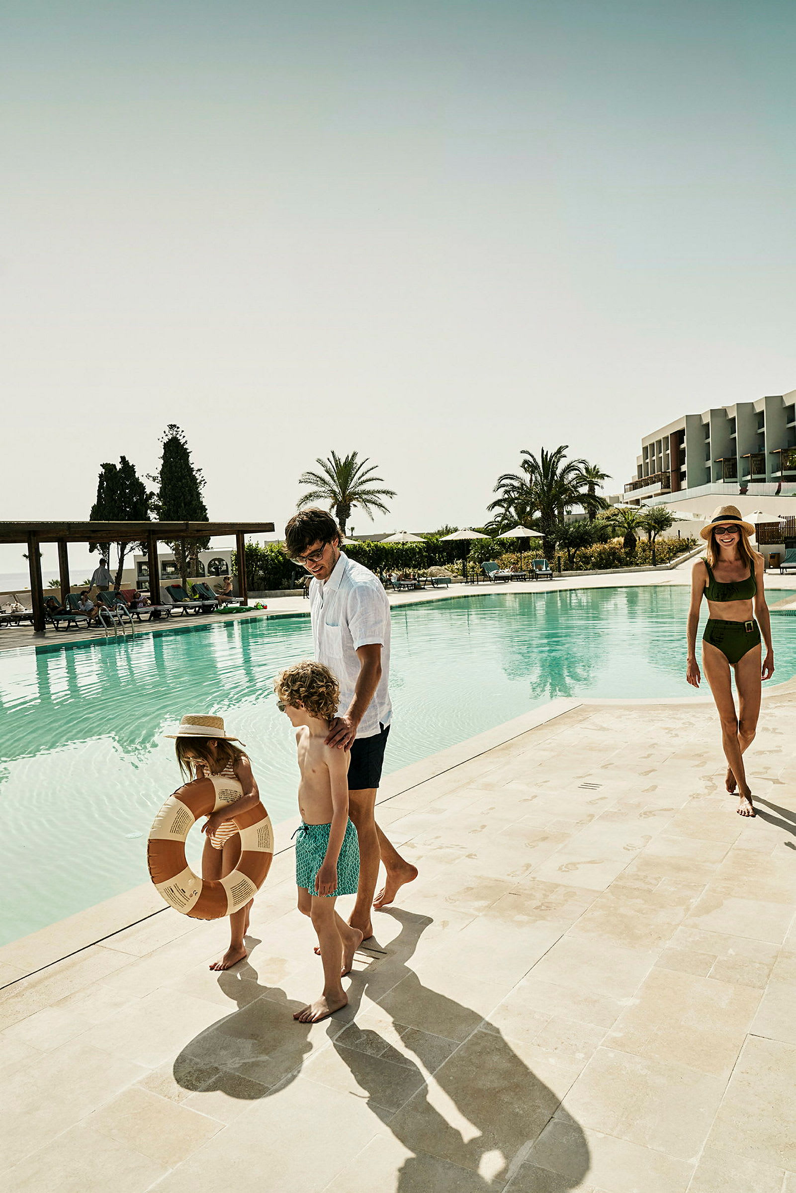 En familj nära en swimmingpool med en byggnad och palmer i bakgrunden. (AI-genererad text)