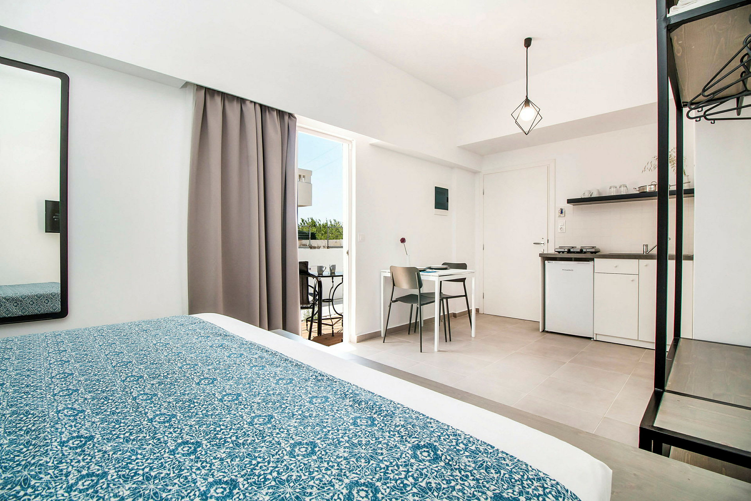 Hotellrum med säng, bord, stolar och ett litet kök. (AI-genererad text)