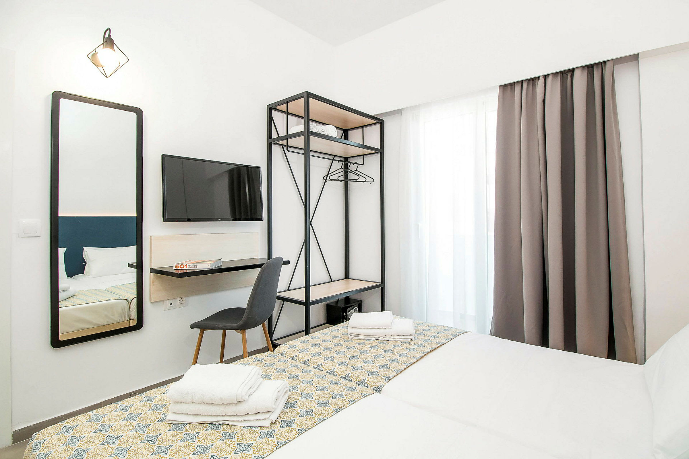 Ett hotellrum med två bäddade sängar, en väggmonterad TV, en spegel och en öppen garderob. (AI-genererad text)