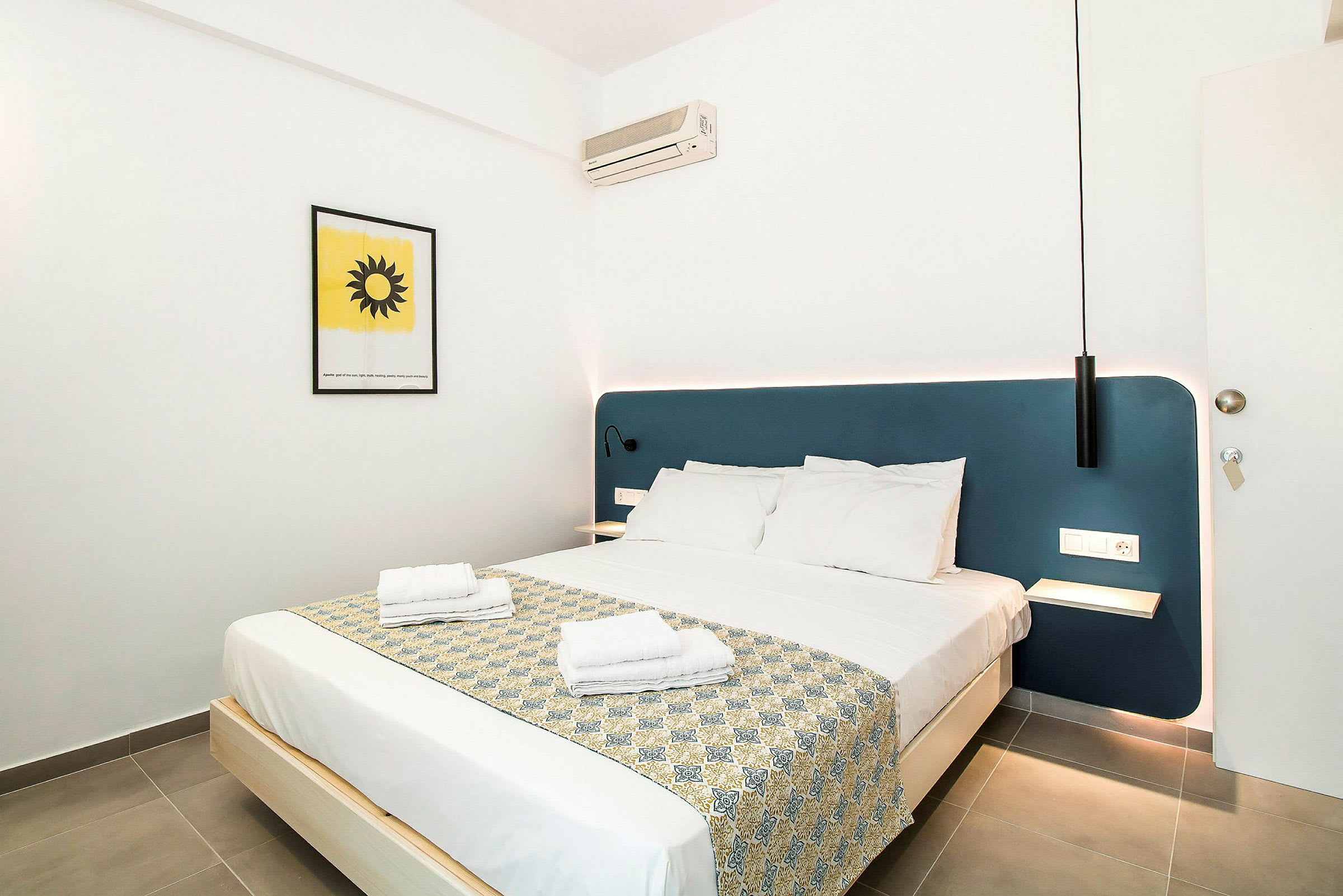 Ett hotellrum med en dubbelbädd, blå sänggavel och väggdekoration. (AI-genererad text)