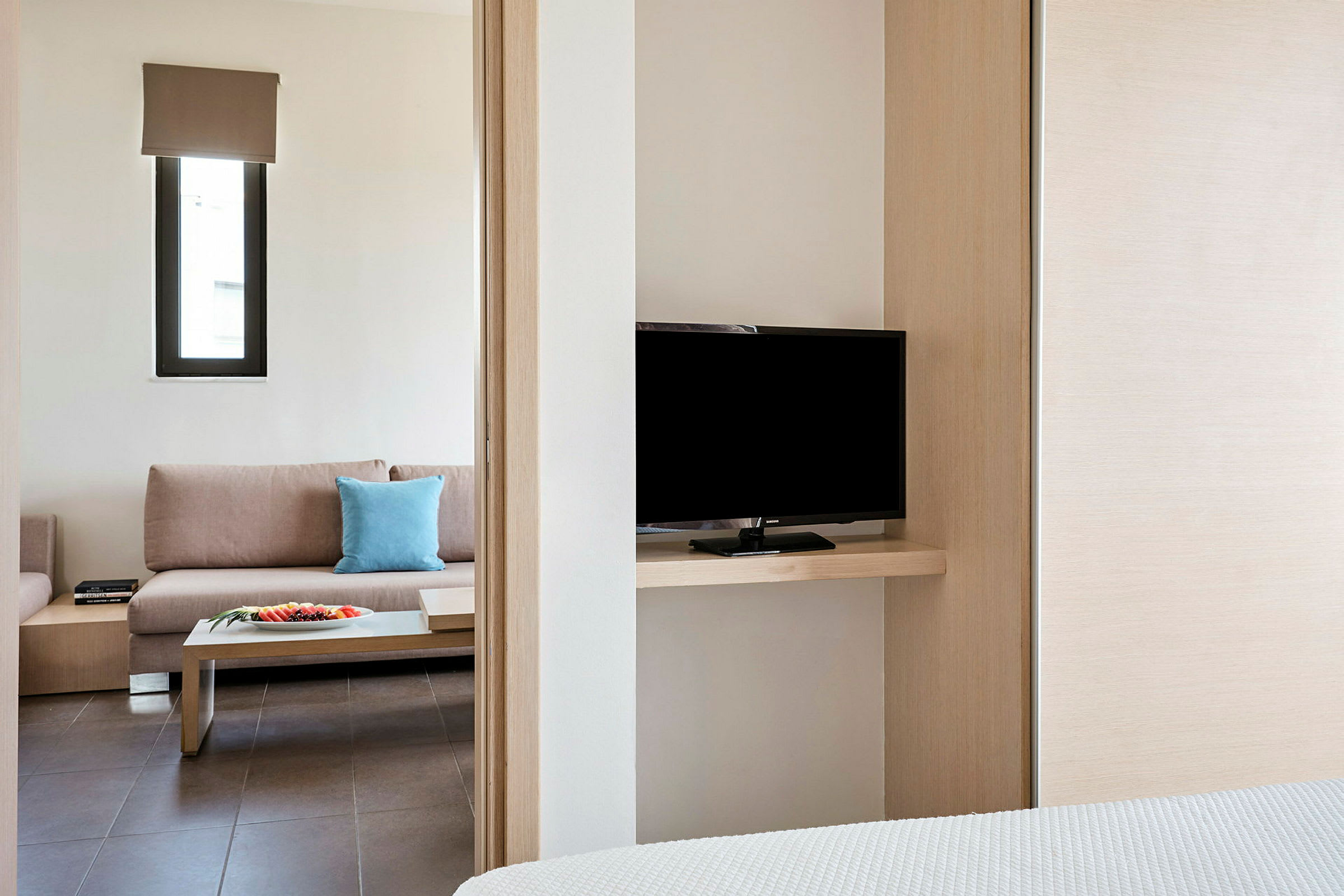 Ett hotellrum med en soffa, ett avlastningsbord och en TV synlig från sovrummet. (AI-genererad text)