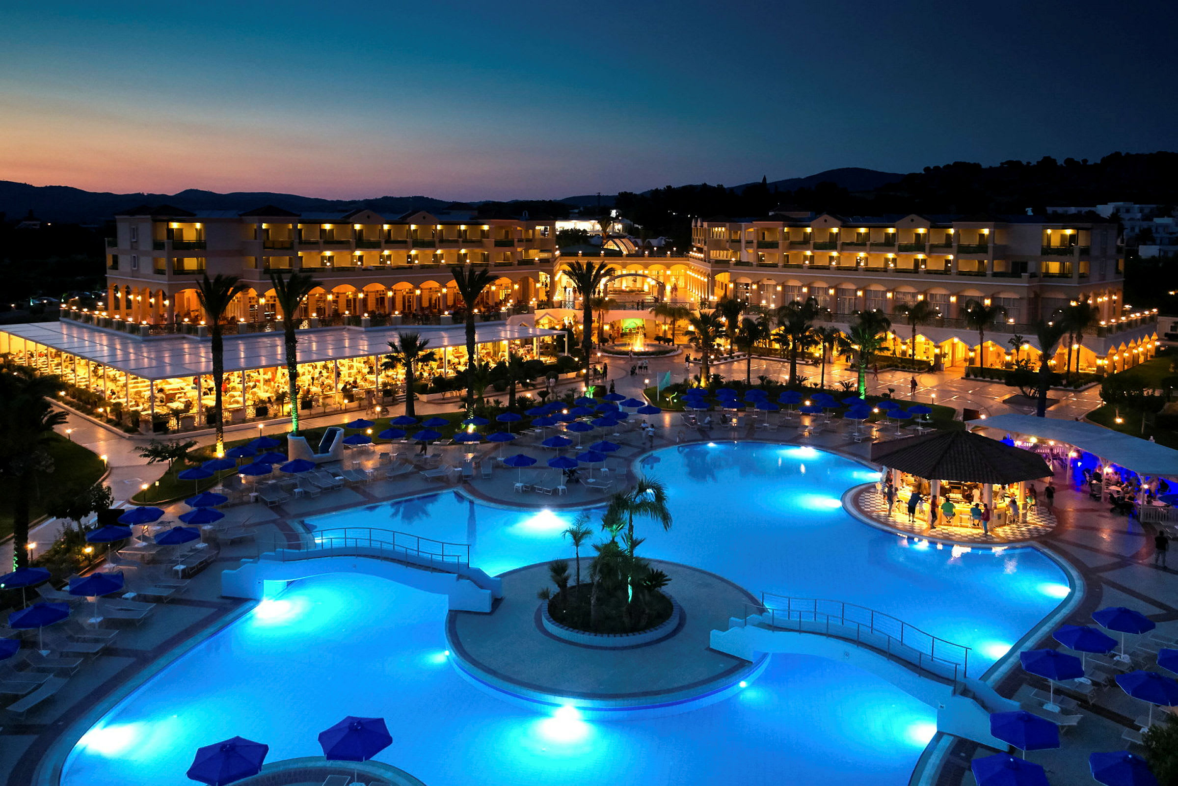 Vy över ett upplyst hotellkomplex med pool på kvällen. (AI-genererad text)