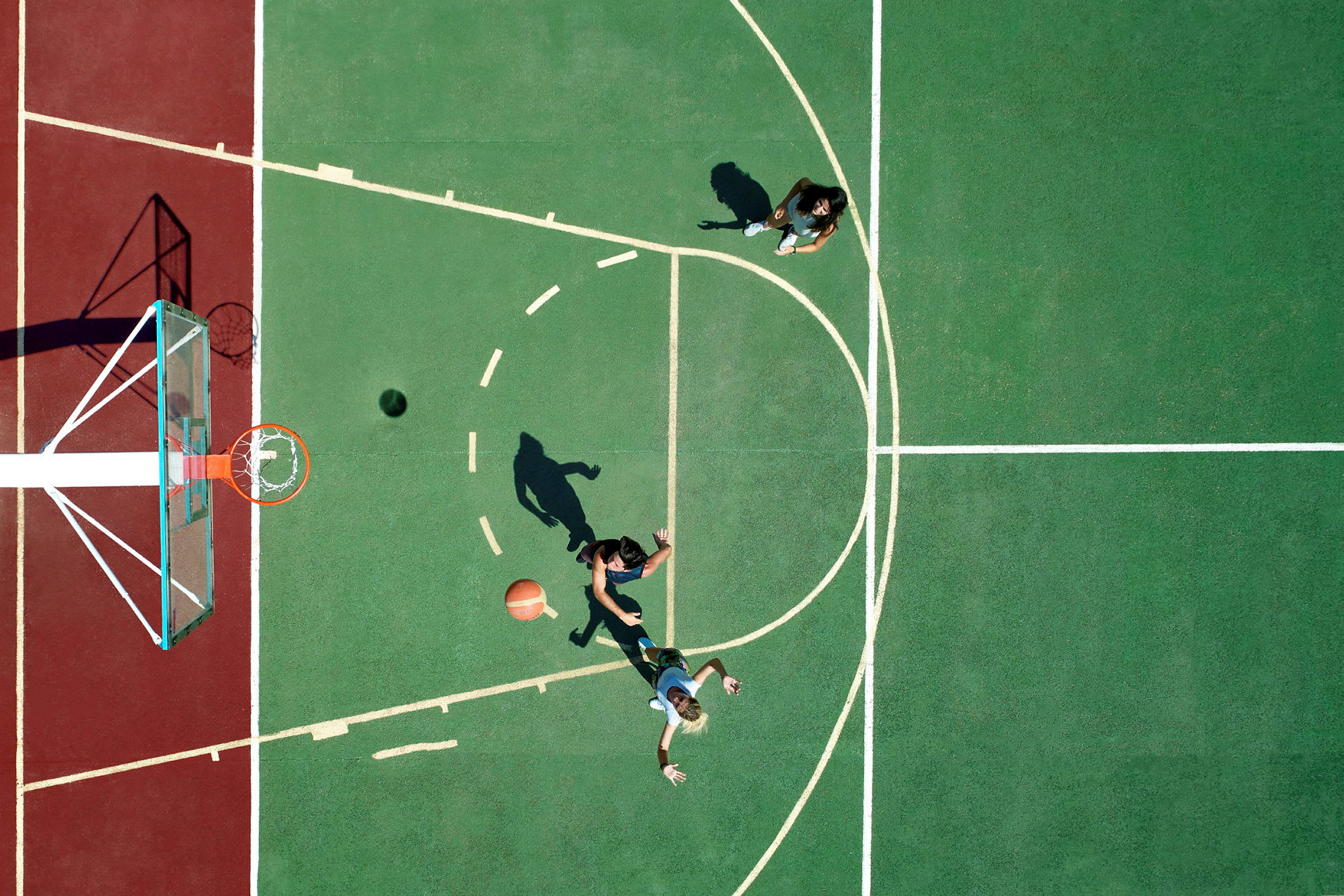 Två personer spelar basket på en utomhusbana, sedd från ovan. (AI-genererad text)