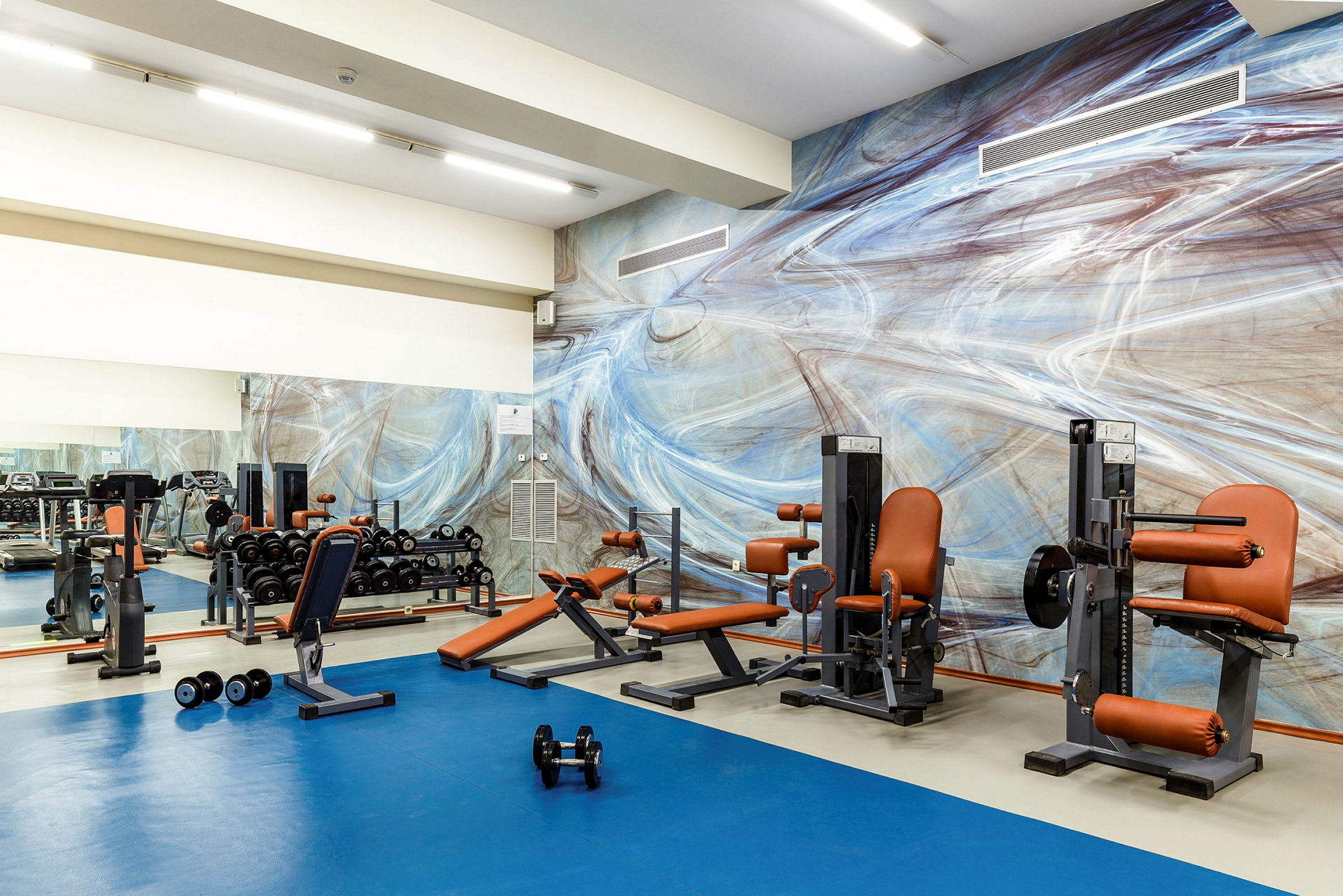 Bild på ett gym med träningsutrustning och en färgglad väggmålning. (AI-genererad text)