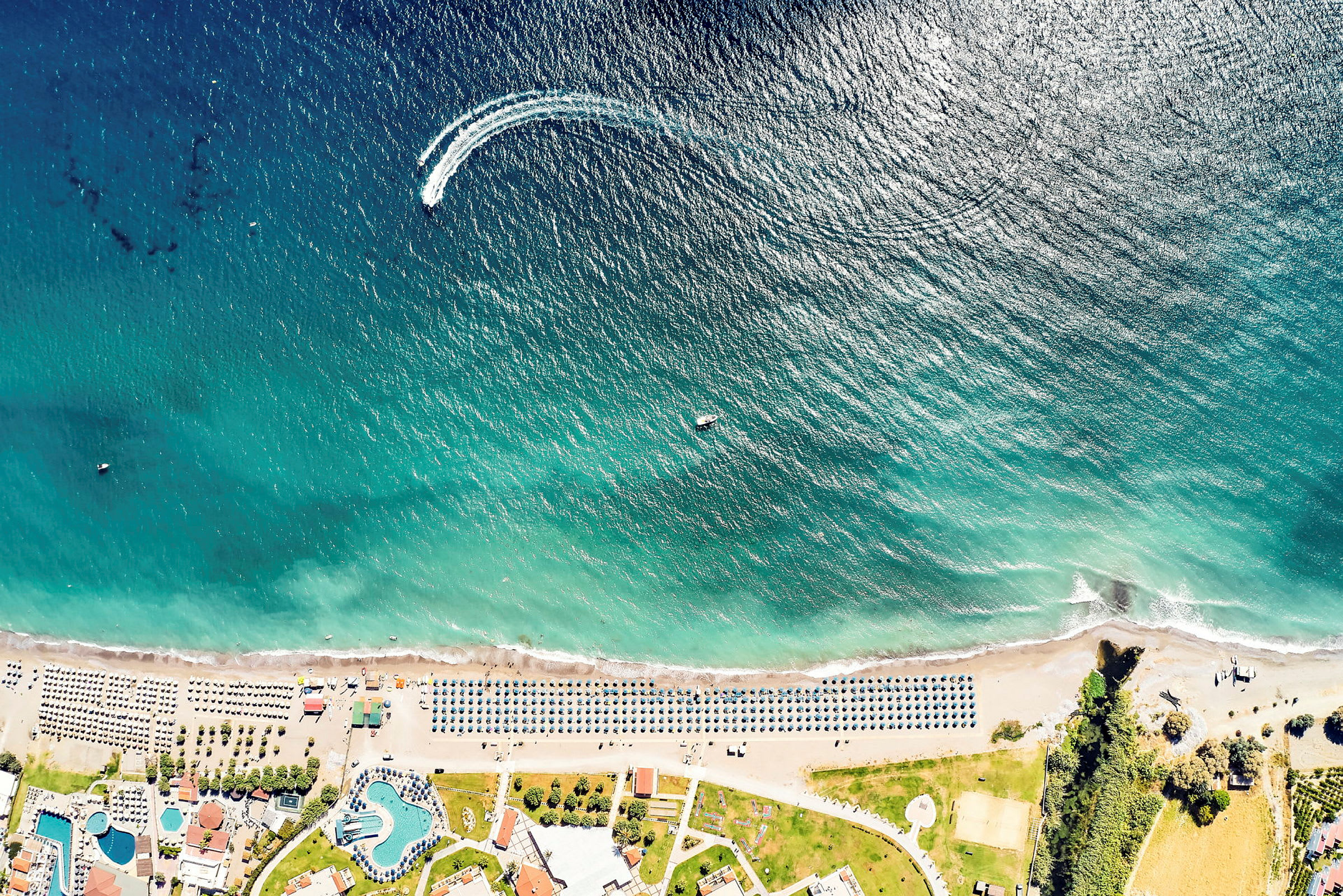 Flygfoto över en strand med parasoller och byggnader vid kusten. (AI-genererad text)