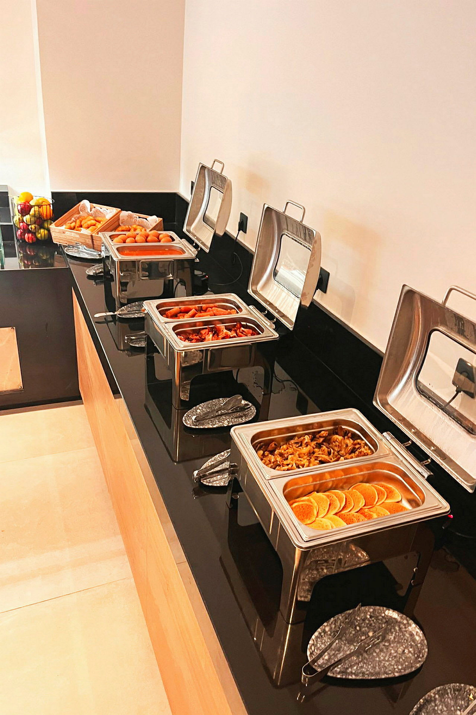 Buffébord med varm mat i serveringskärl och färska frukter vid sidan av. (AI-genererad text)