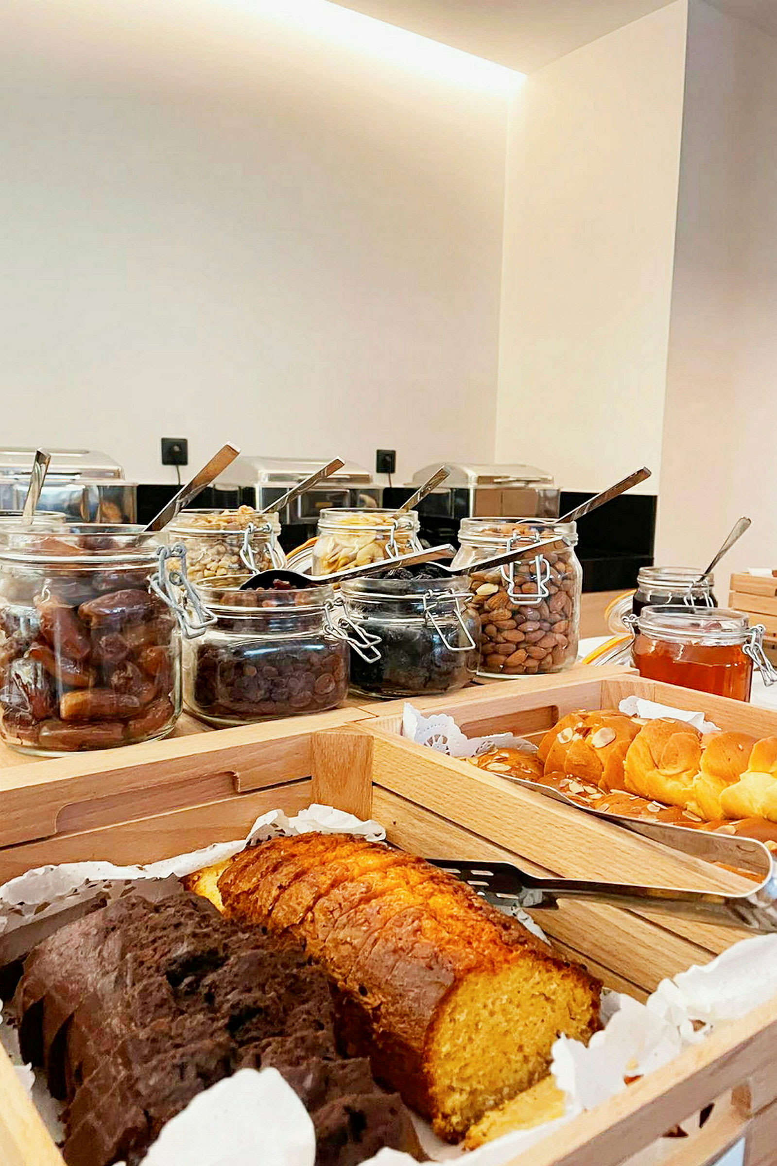 Bild på en frukostbuffé med olika bröd, bakverk och burkar fyllda med nötter och torkad frukt. (AI-genererad text)