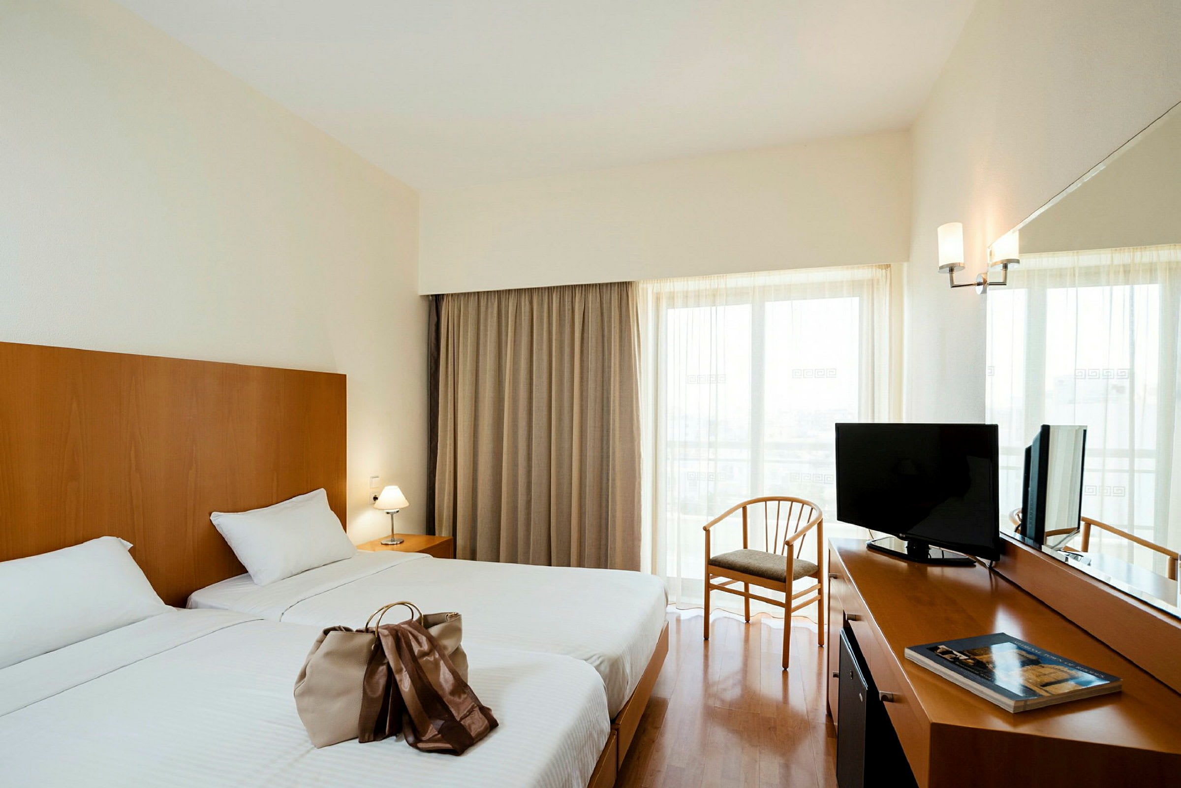Hotellrum med två enkelsängar, ett skrivbord med TV och en stol framför ett fönster med gardiner. (AI-genererad text)