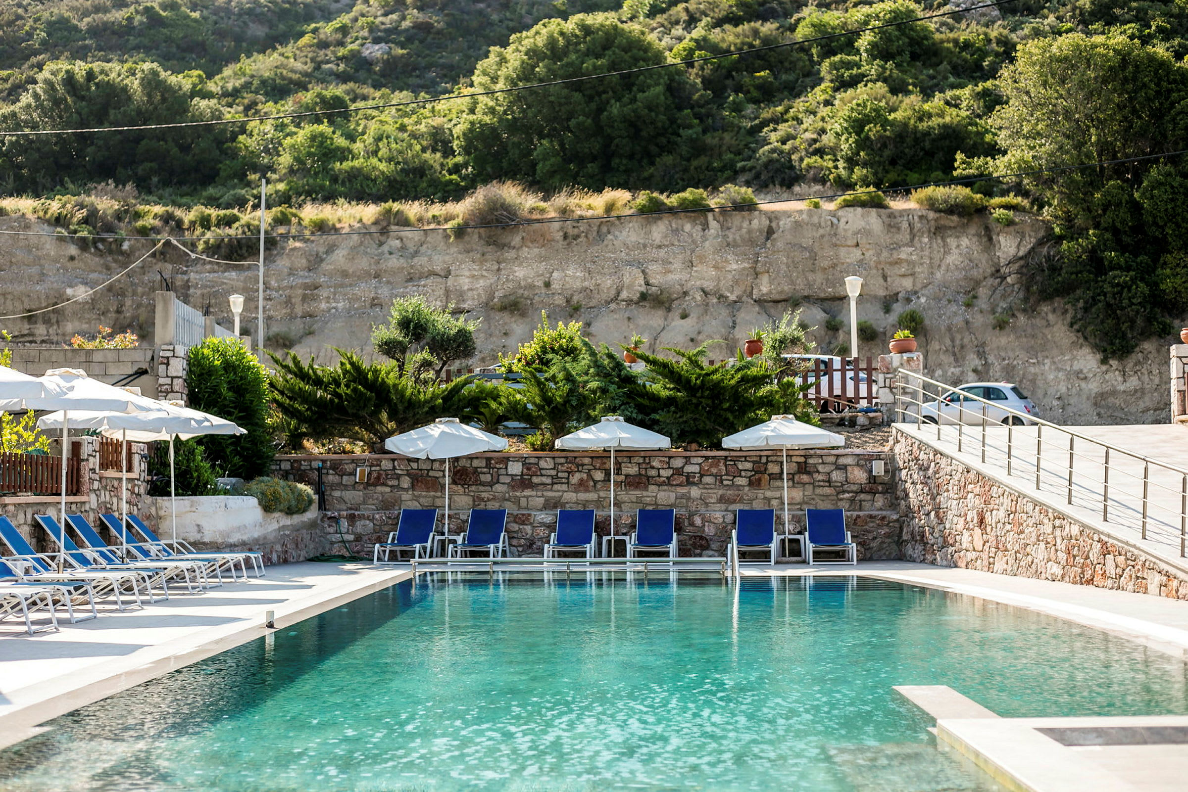 Pool med solsängar, parasoller och grönska i bakgrunden. (AI-genererad text)
