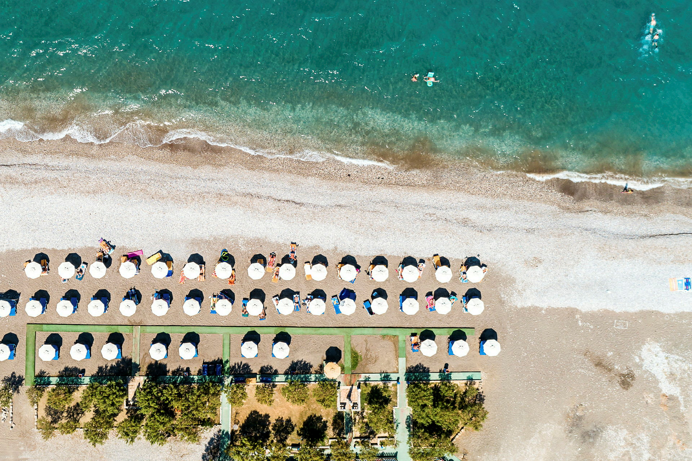 Flygbild av en strand med parasoller och stolar nära vattnet. (AI-genererad text)