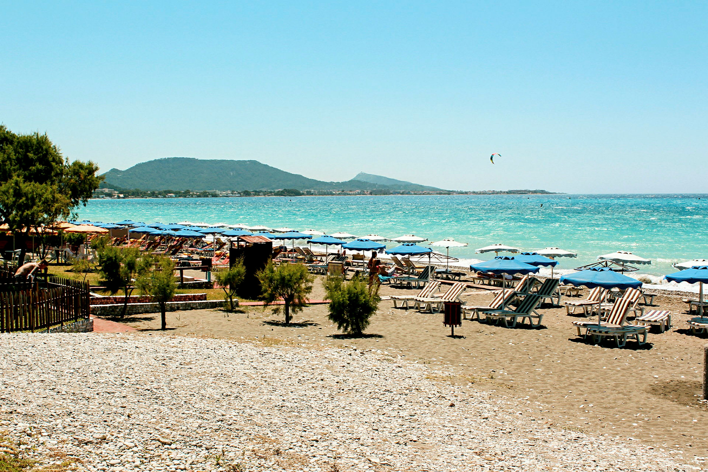Strand med solstolar, parasoller och blått hav i bakgrunden. (AI-genererad text)