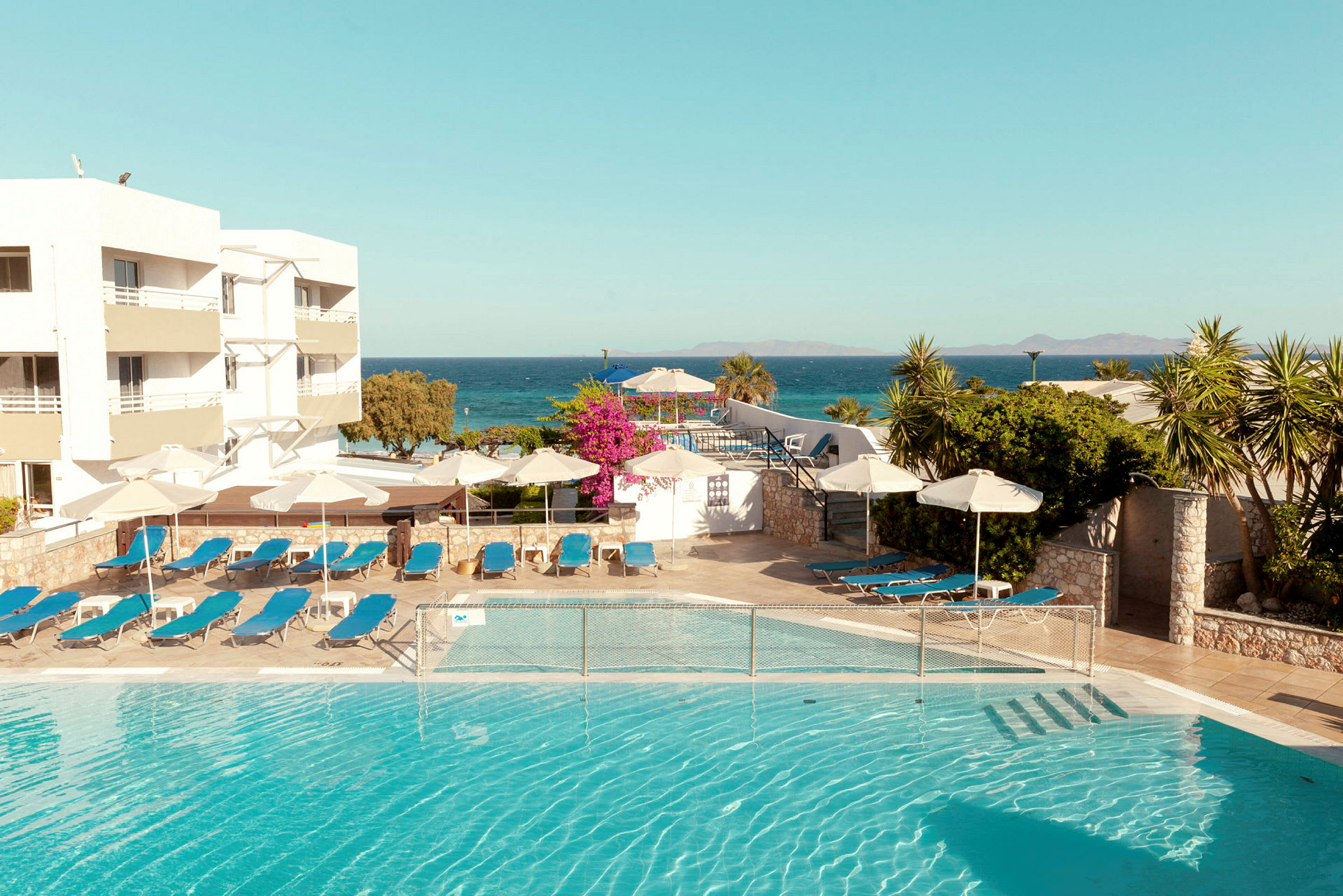 En utomhuspool med solstolar och parasoller vid sidan av ett hotell vid havet. (AI-genererad text)