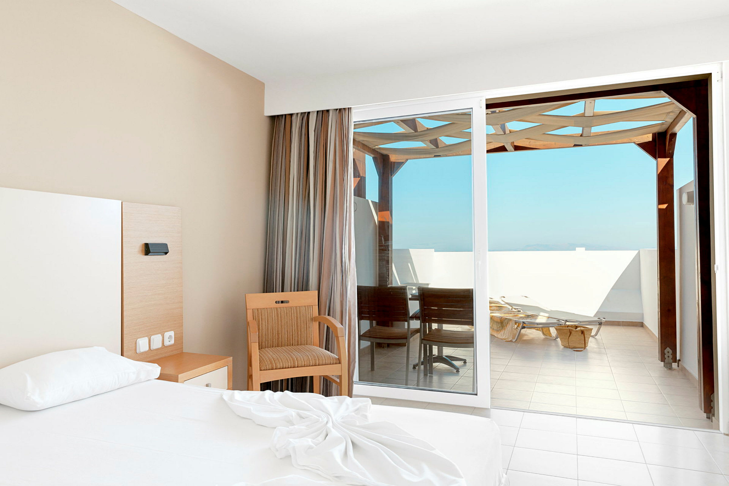 En hotellrum med en säng, stol och utgång till en balkong med solstolar. (AI-genererad text)