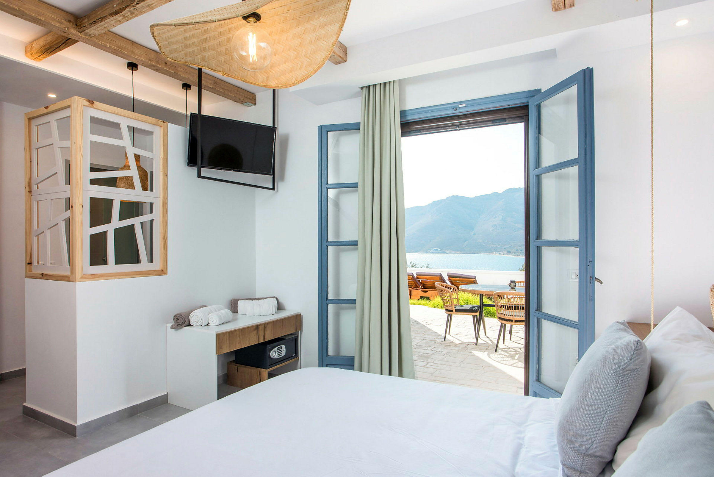 Hotellrum med öppna dörrar till terrass och havsutsikt. (AI-genererad text)