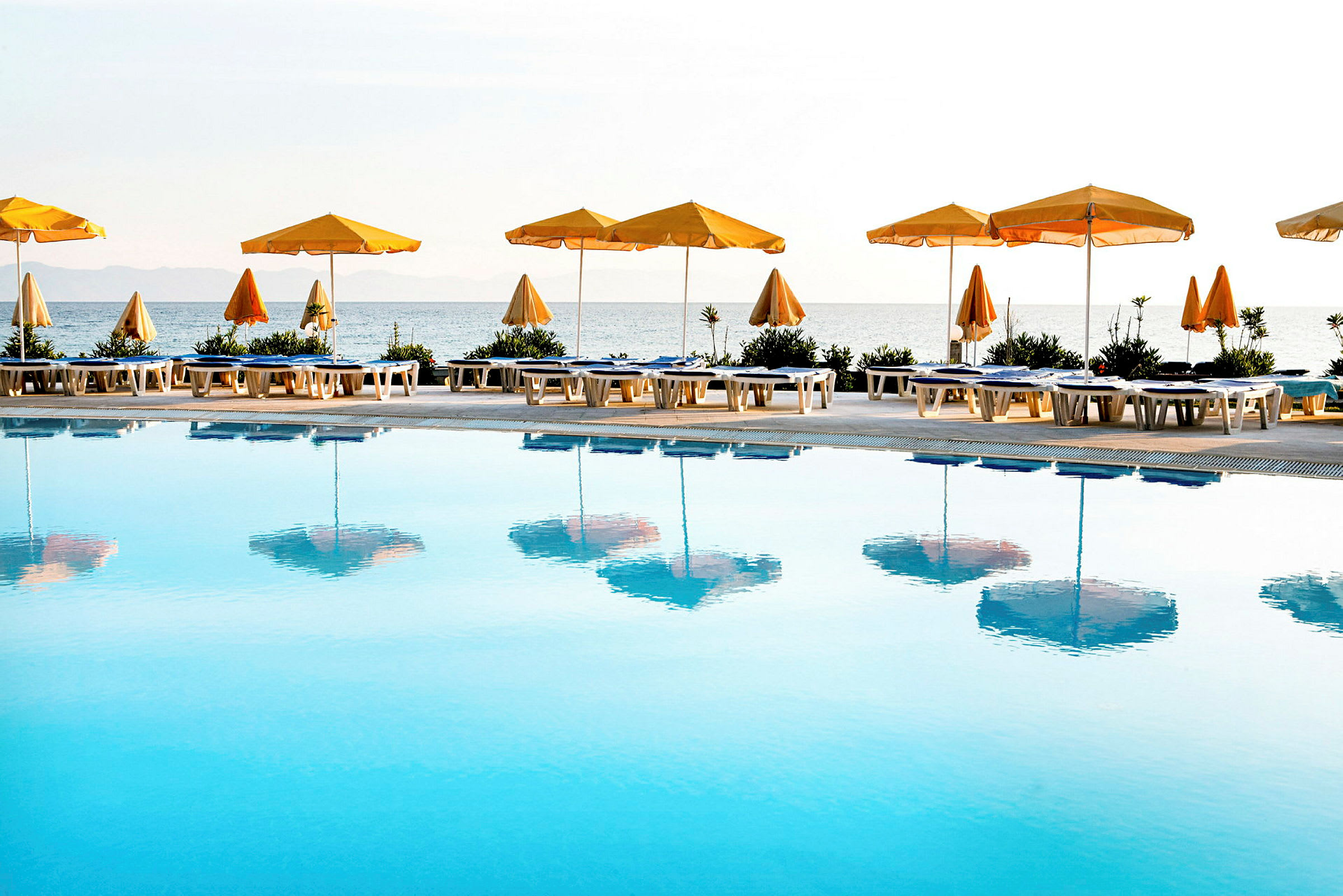 En utomhuspool med gula parasoller och solstolar framför havet. (AI-genererad text)