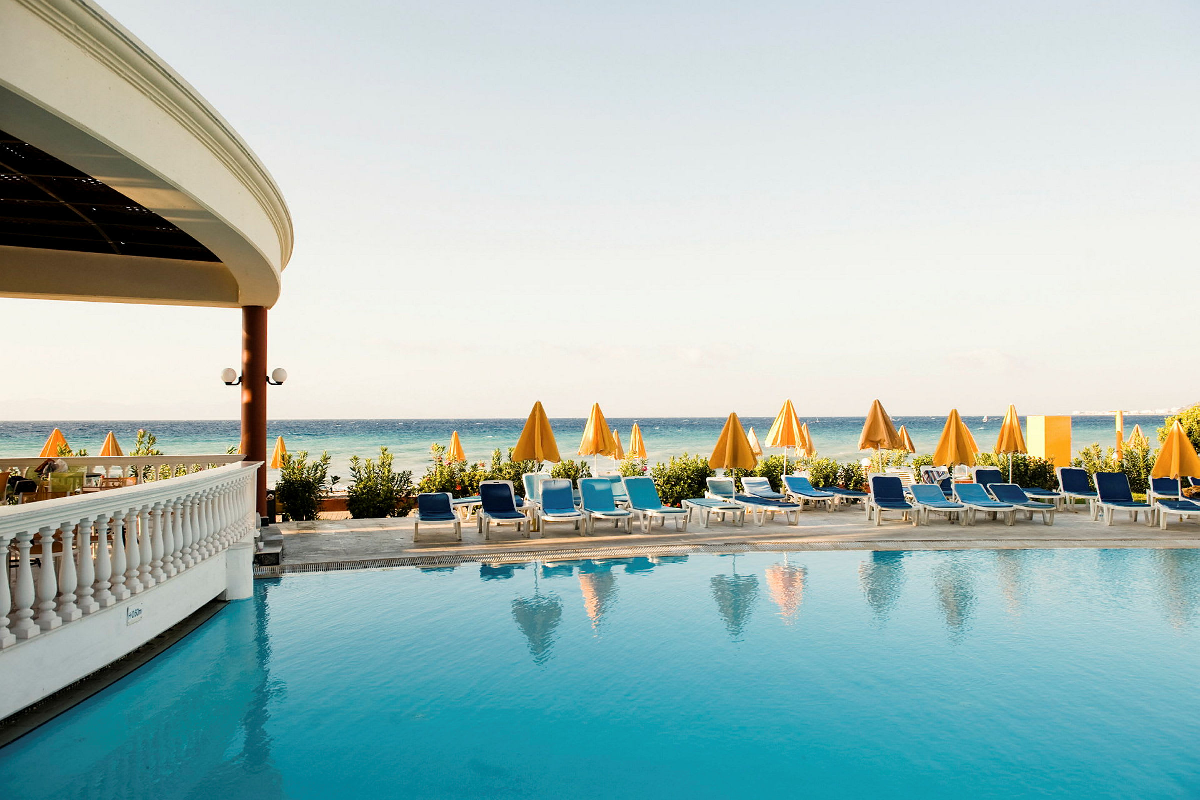 En pool med solstolar och gula parasoller framför havet. (AI-genererad text)