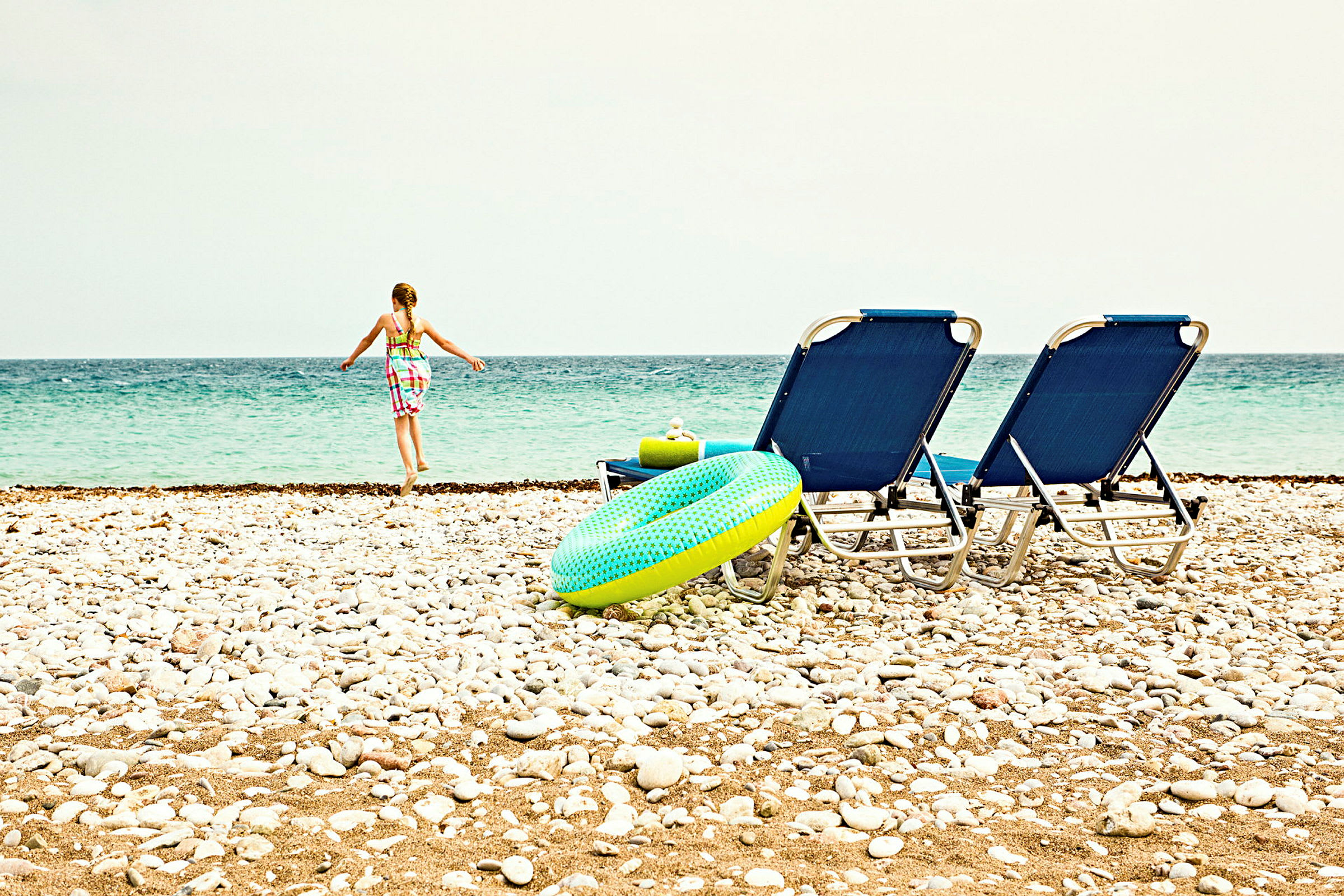 En strand med stolar, en badring och en person som går mot havet. (AI-genererad text)