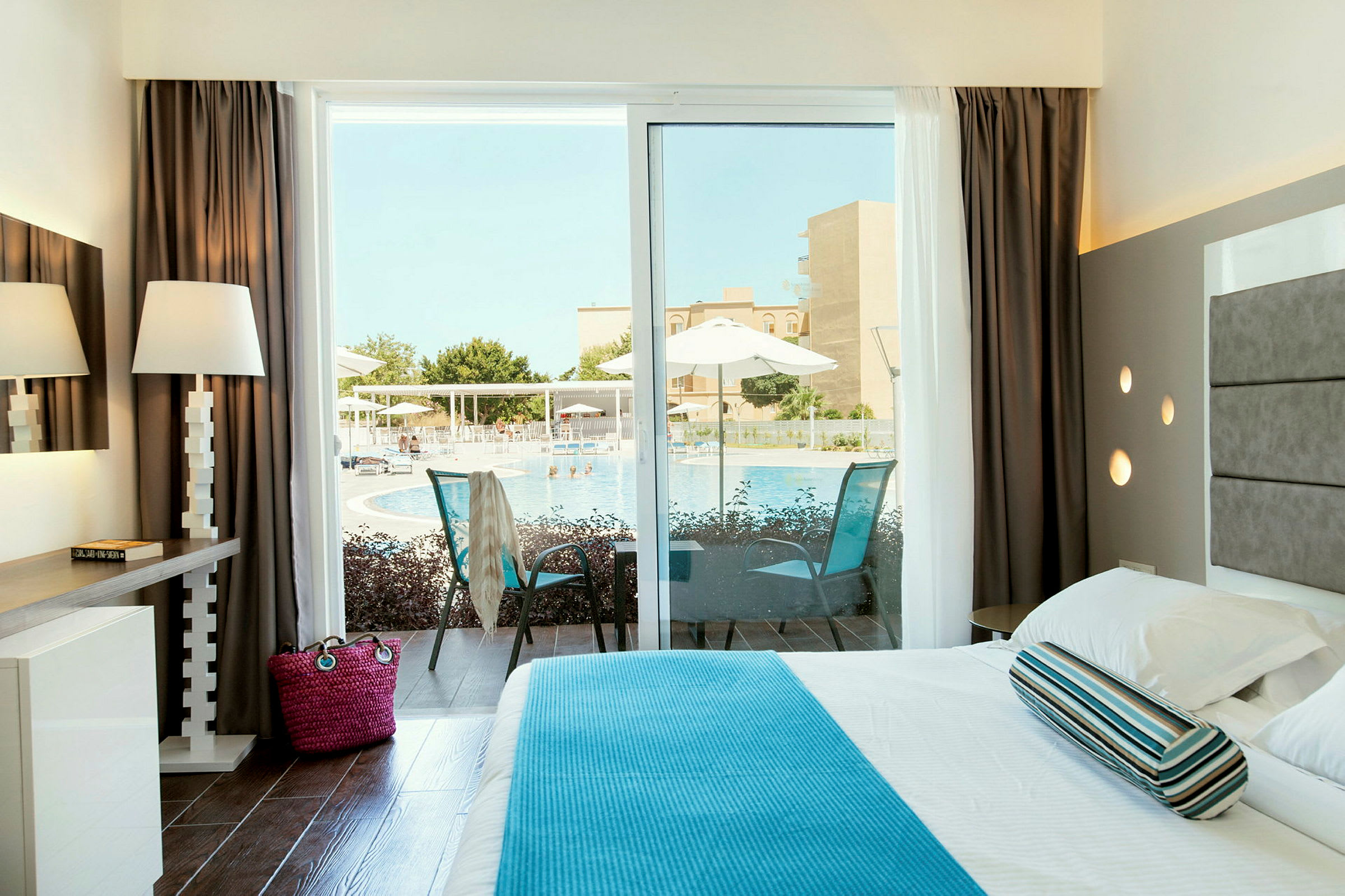 Ett ljust hotellrum med utsikt över en pool genom en glasdörr. (AI-genererad text)