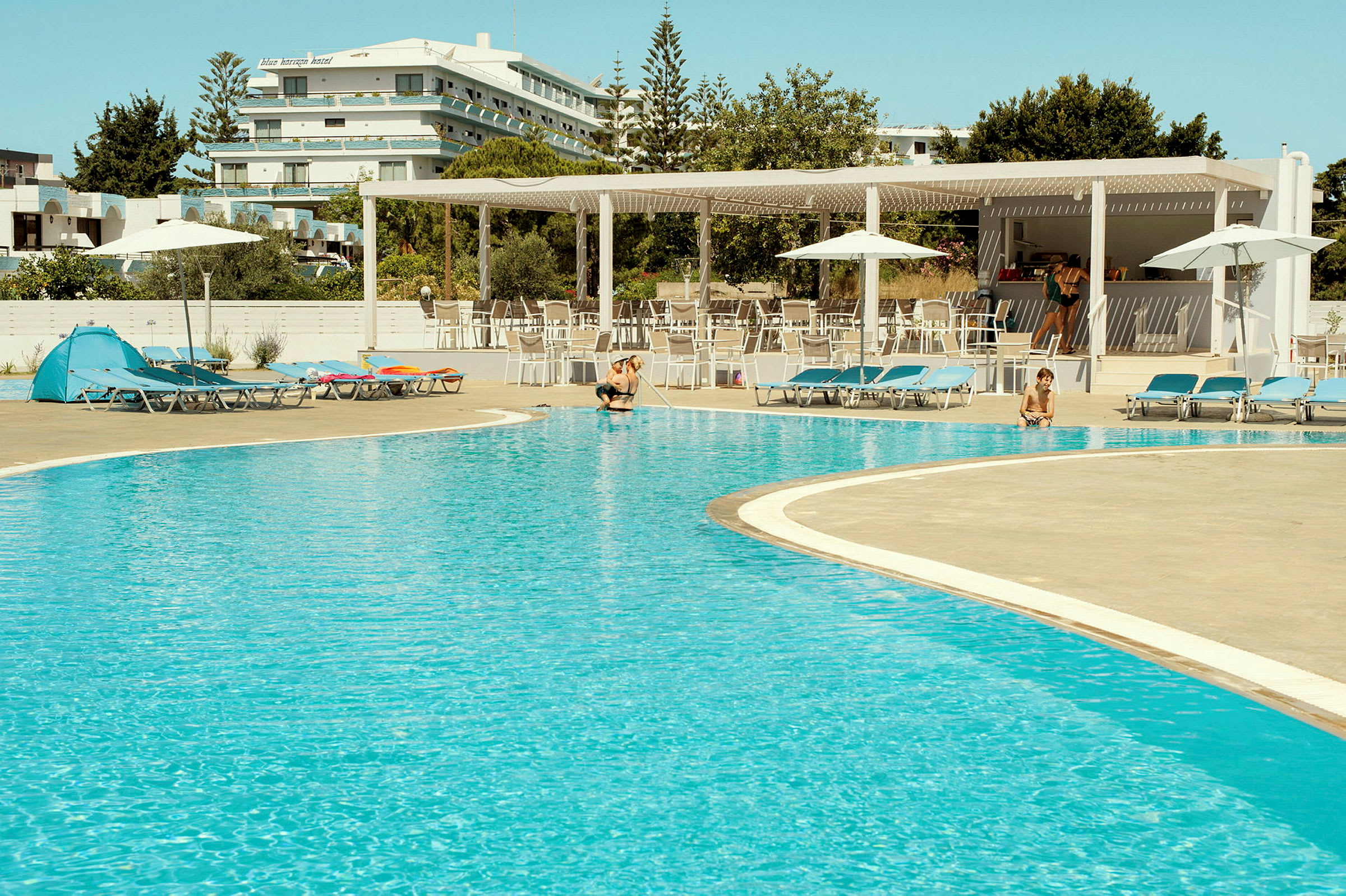 En utomhuspool vid ett hotell, omgiven av solstolar och parasoller. (AI-genererad text)