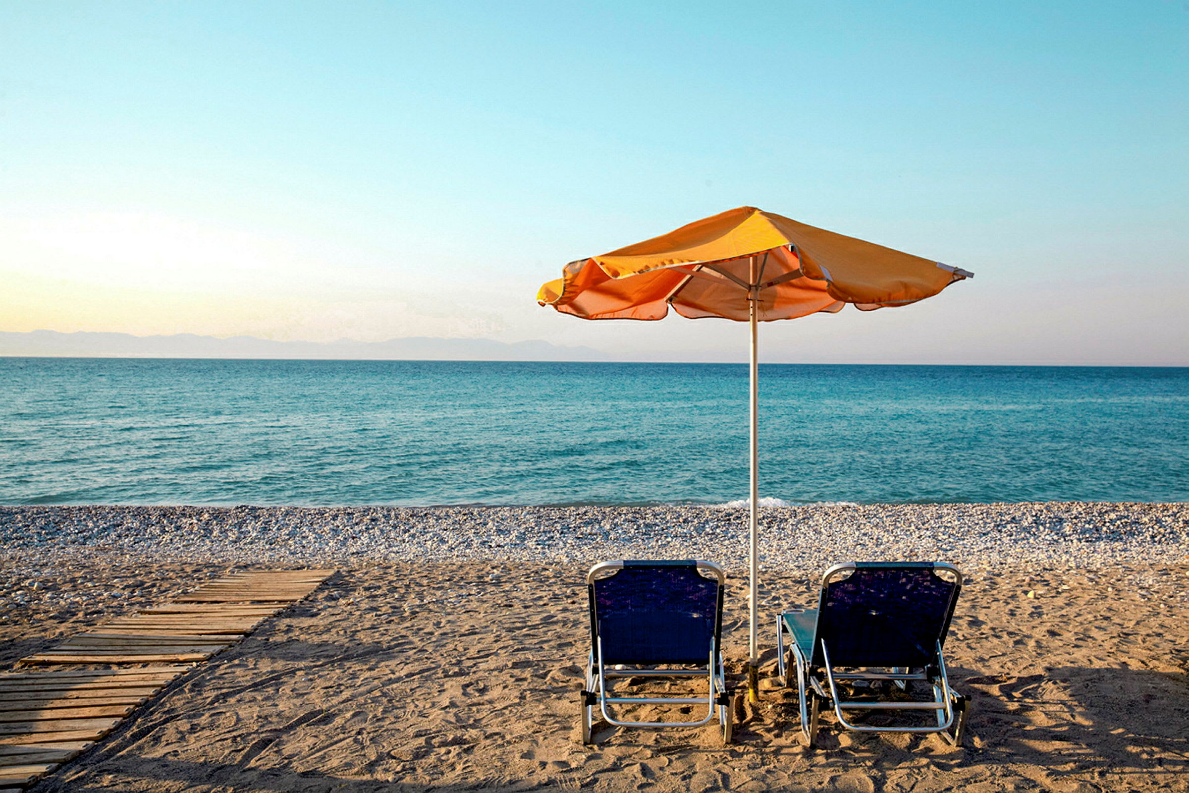 Två solstolar och ett parasoll på en strand med utsikt över havet. (AI-genererad text)