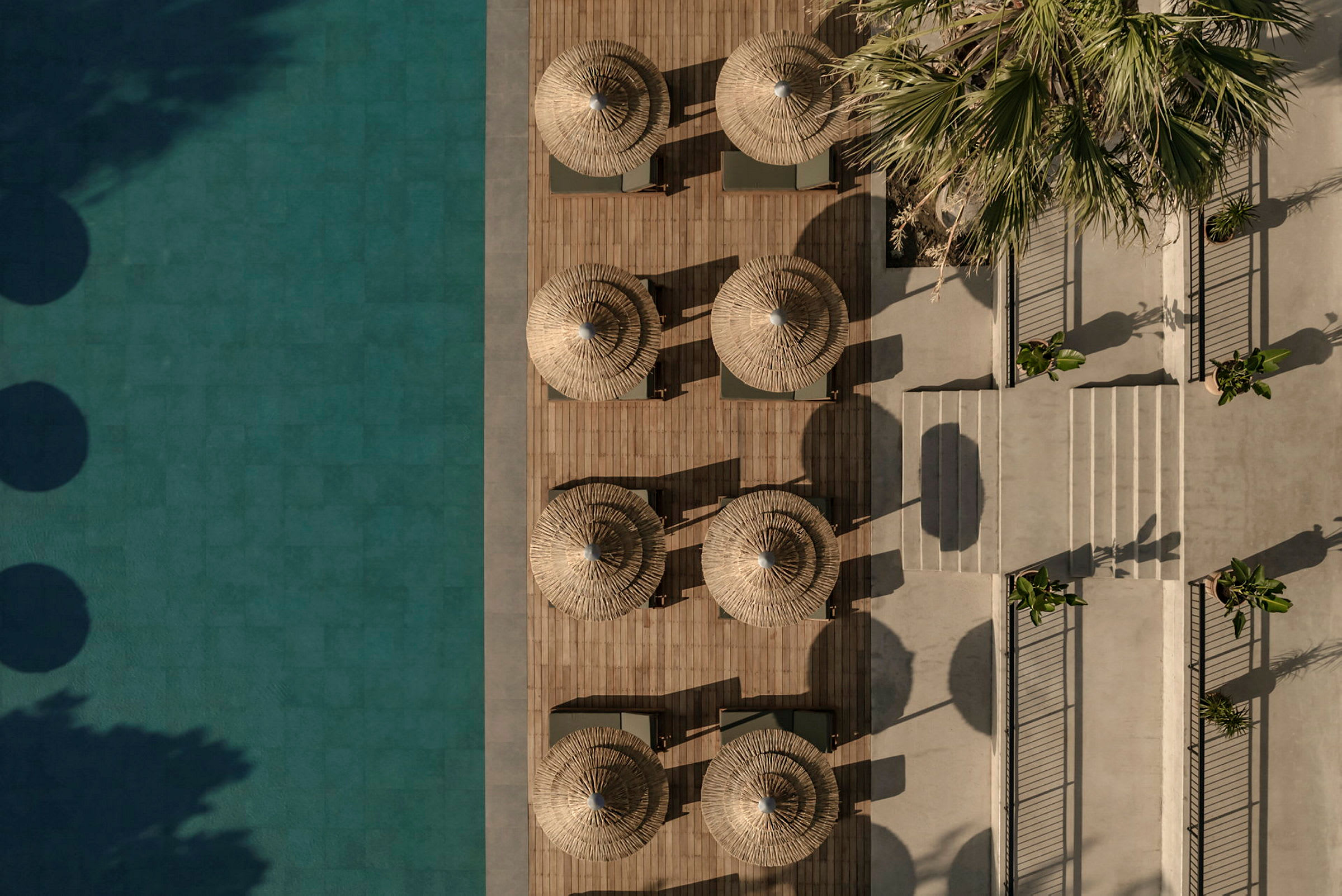 Flygfoto av solstolar och parasoller vid en pool, med träd och växtlighet i närheten. (AI-genererad text)
