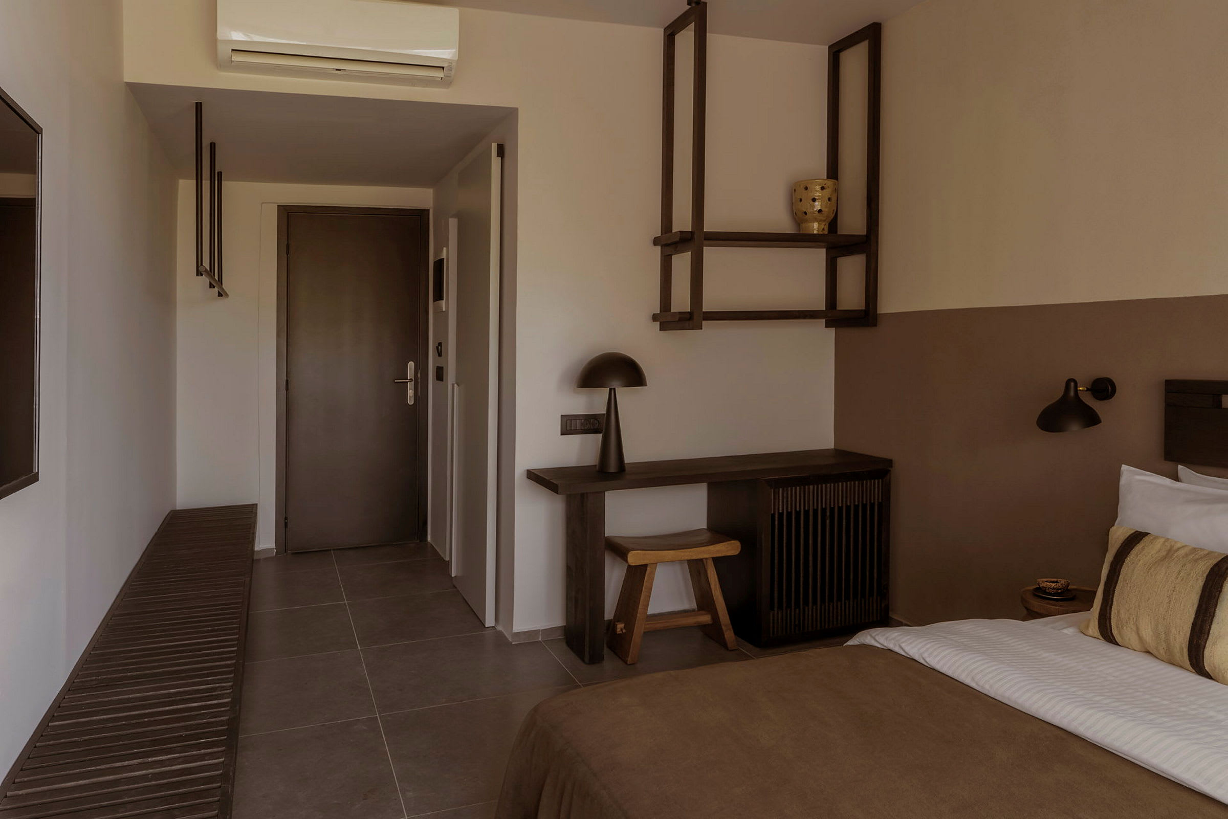 Ett hotellrum med dörr, skrivbord, säng och dekorativa hyllor. (AI-genererad text)