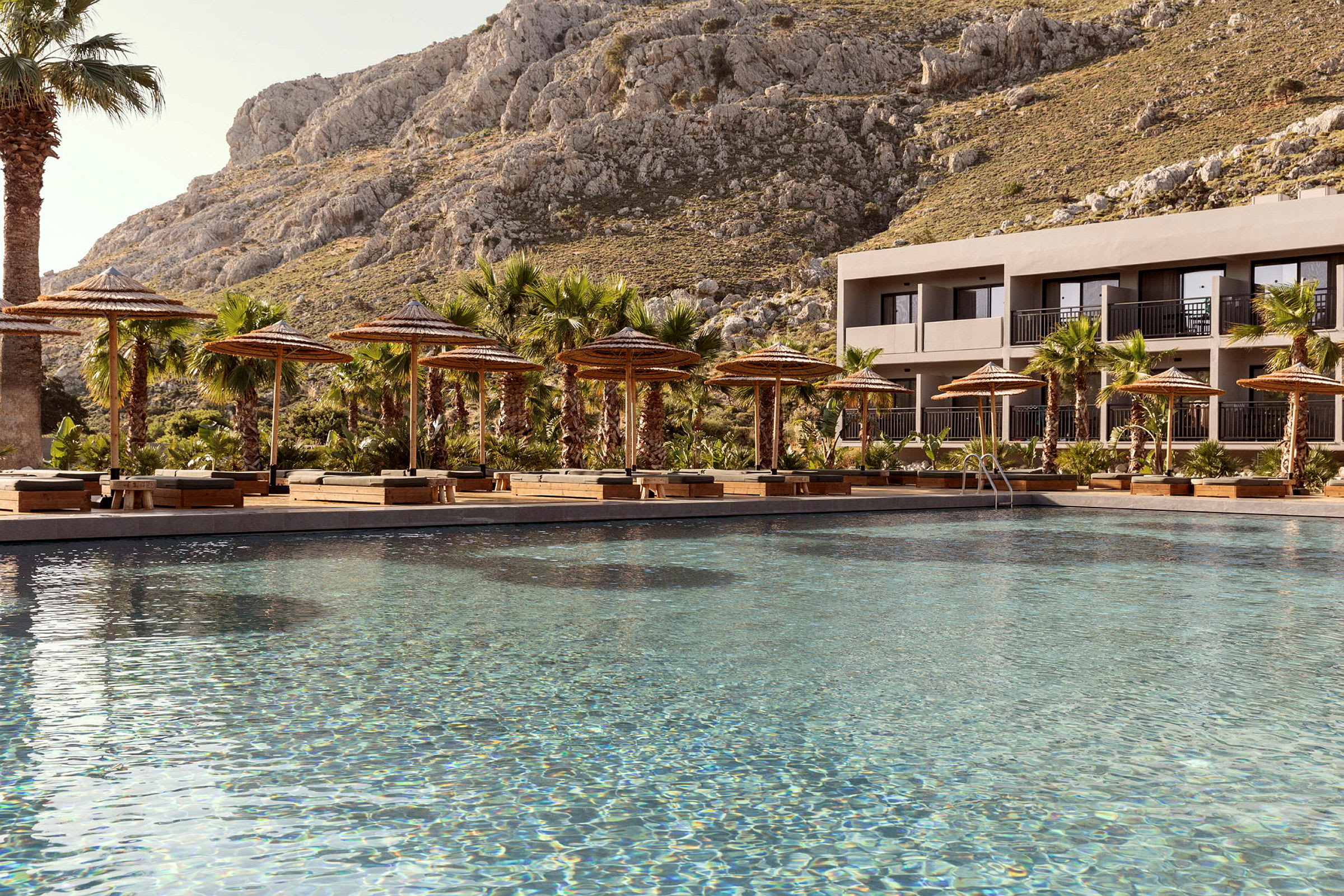 Pool med solstolar och parasoll samt berg i bakgrunden. (AI-genererad text)