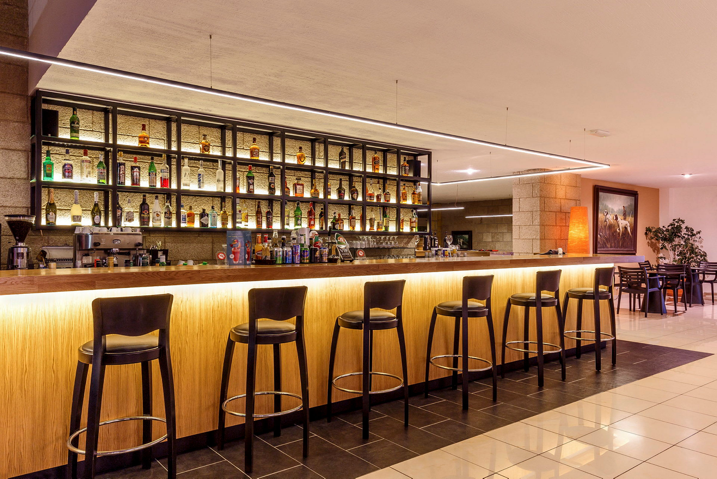 En modern bar med höga stolar och hyllor med olika flaskor. (AI-genererad text)