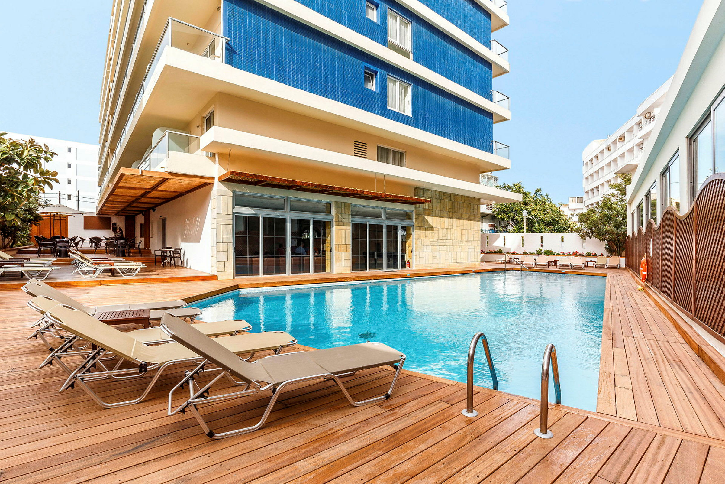 Utomhuspool med solstolar och hotellbyggnaden i bakgrunden. (AI-genererad text)