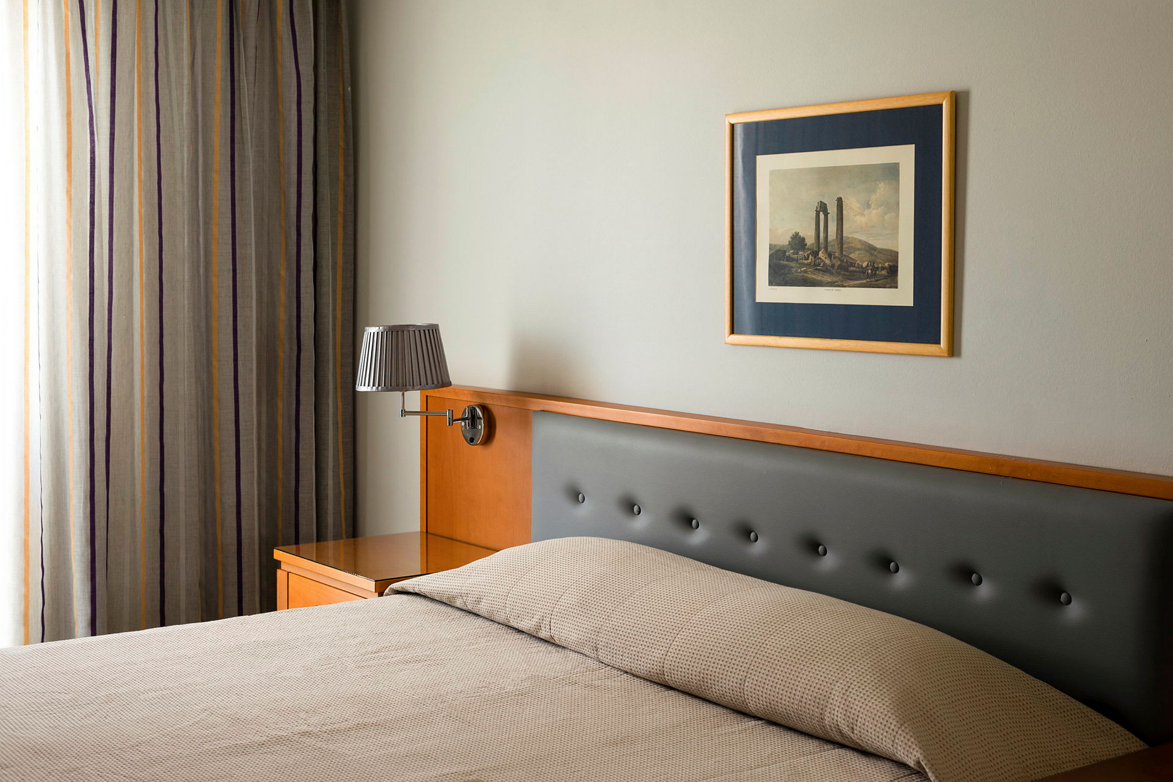 Ett hotellrum med säng, vägglampa och tavla. (AI-genererad text)