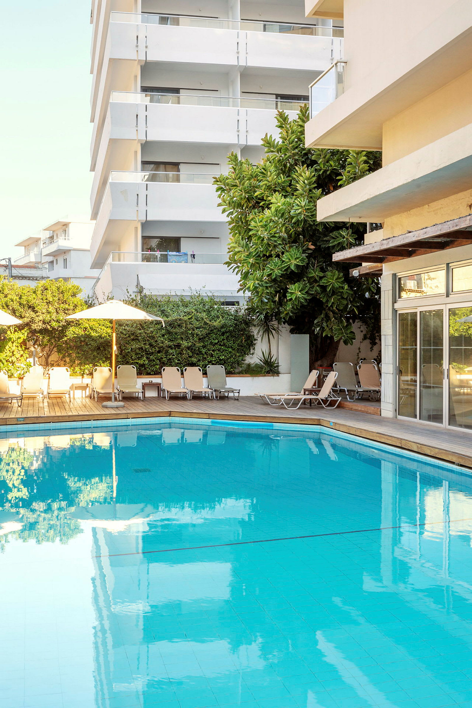 Utomhuspool med solstolar och hotellbyggnad i bakgrunden. (AI-genererad text)