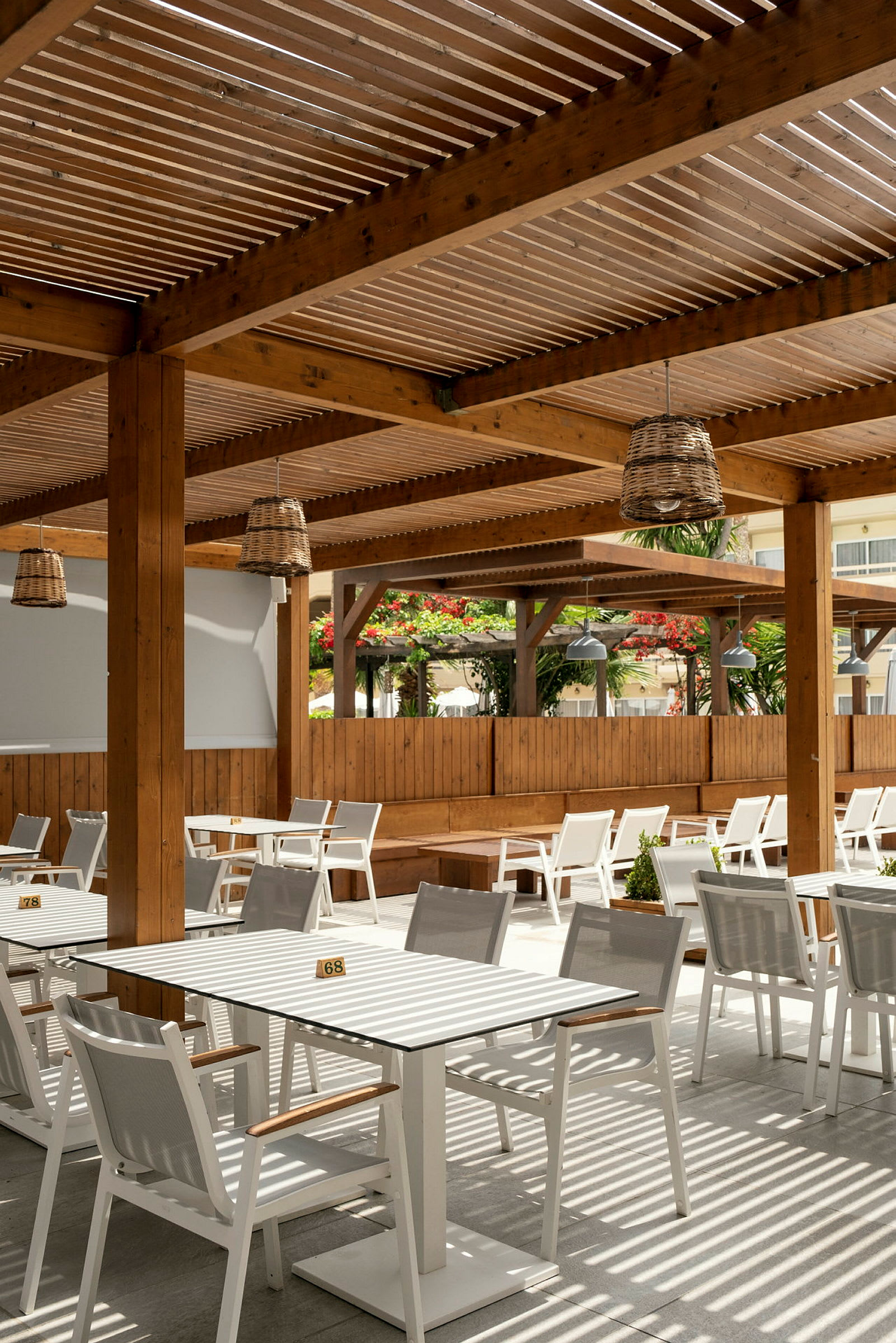 Uteservering med bord och stolar under en träpergola. (AI-genererad text)