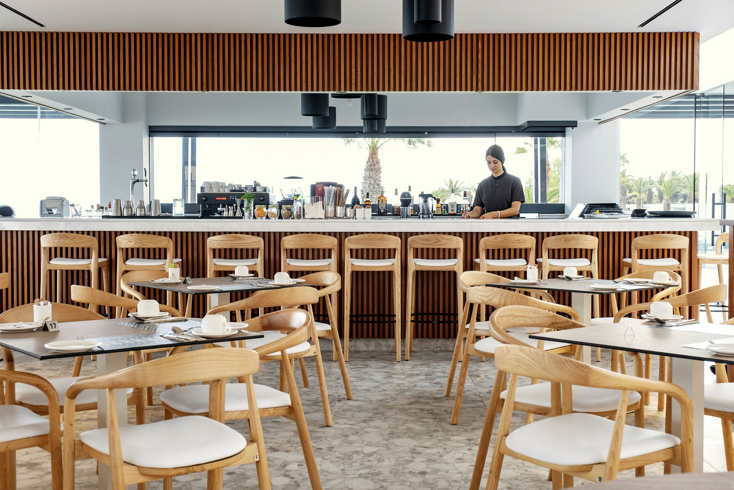 Restaurang med trästolar, bord och en lång bardisk med drycker. (AI-genererad text)