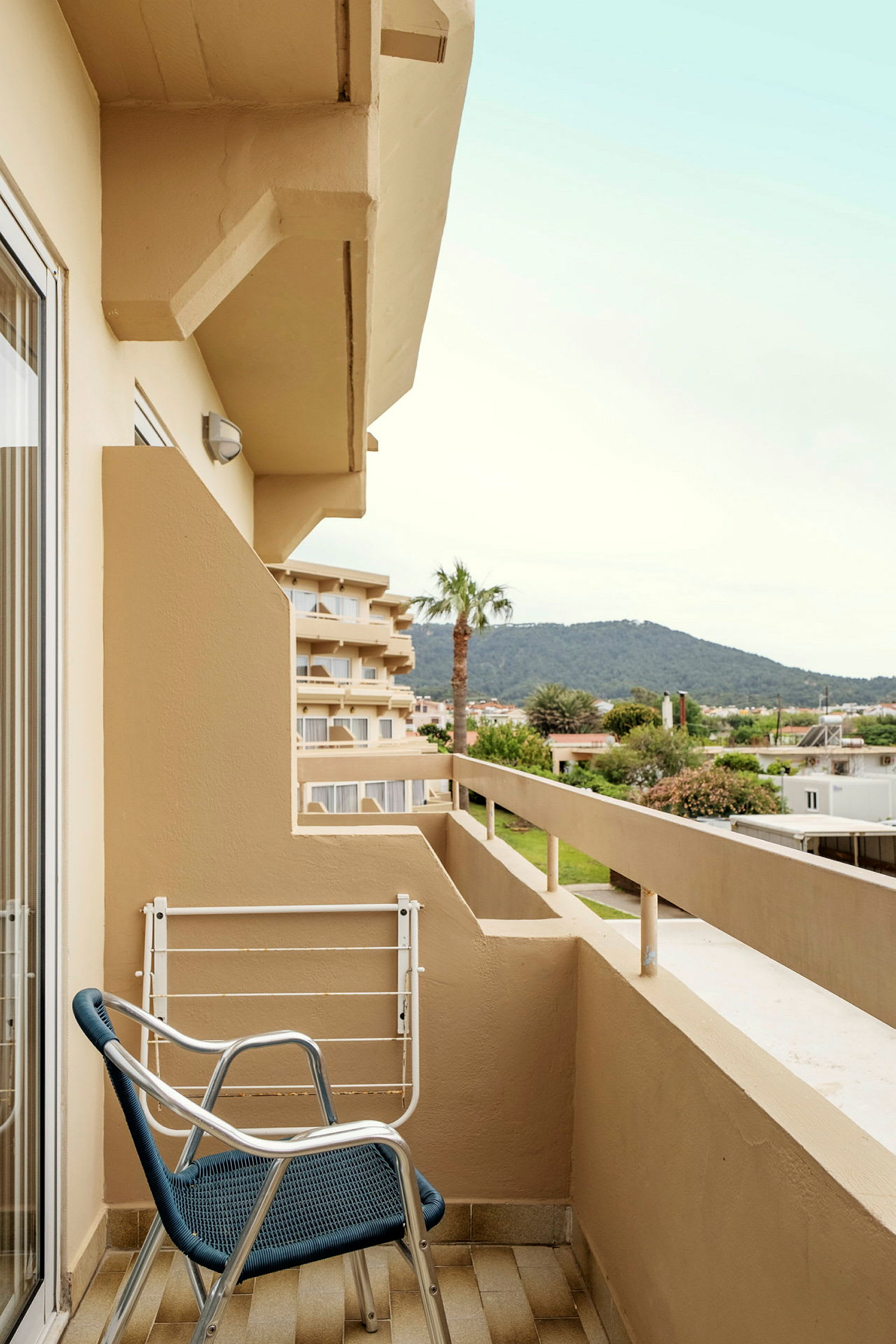 Balkong med stol och utsikt över hotellbyggnader, grönska och berg. (AI-genererad text)