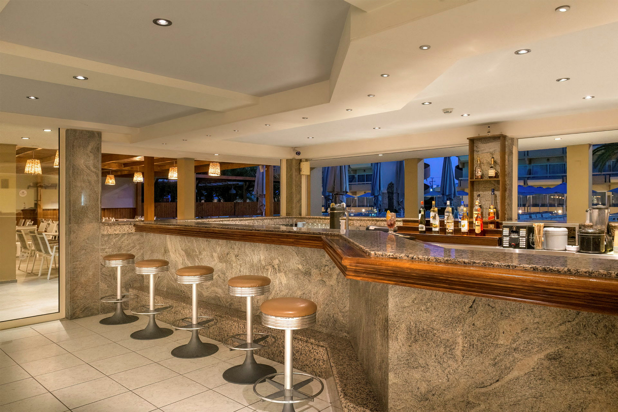 En hotellbar med flera sittplatser och en granitbänkskiva, synliga drinkflaskor och stolar. (AI-genererad text)