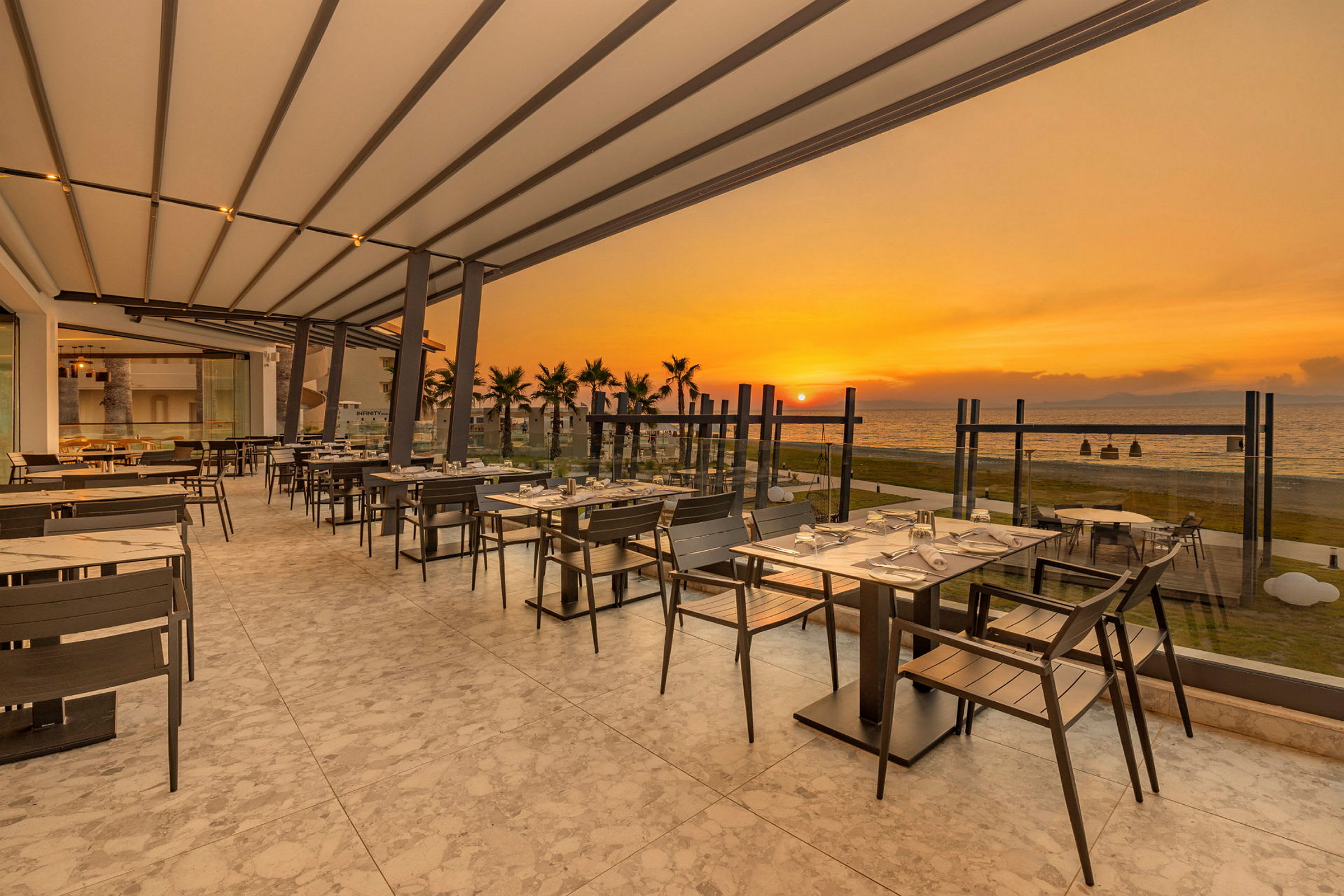 En utomhusrestaurang med utsikt över havet vid solnedgång. (AI-genererad text)