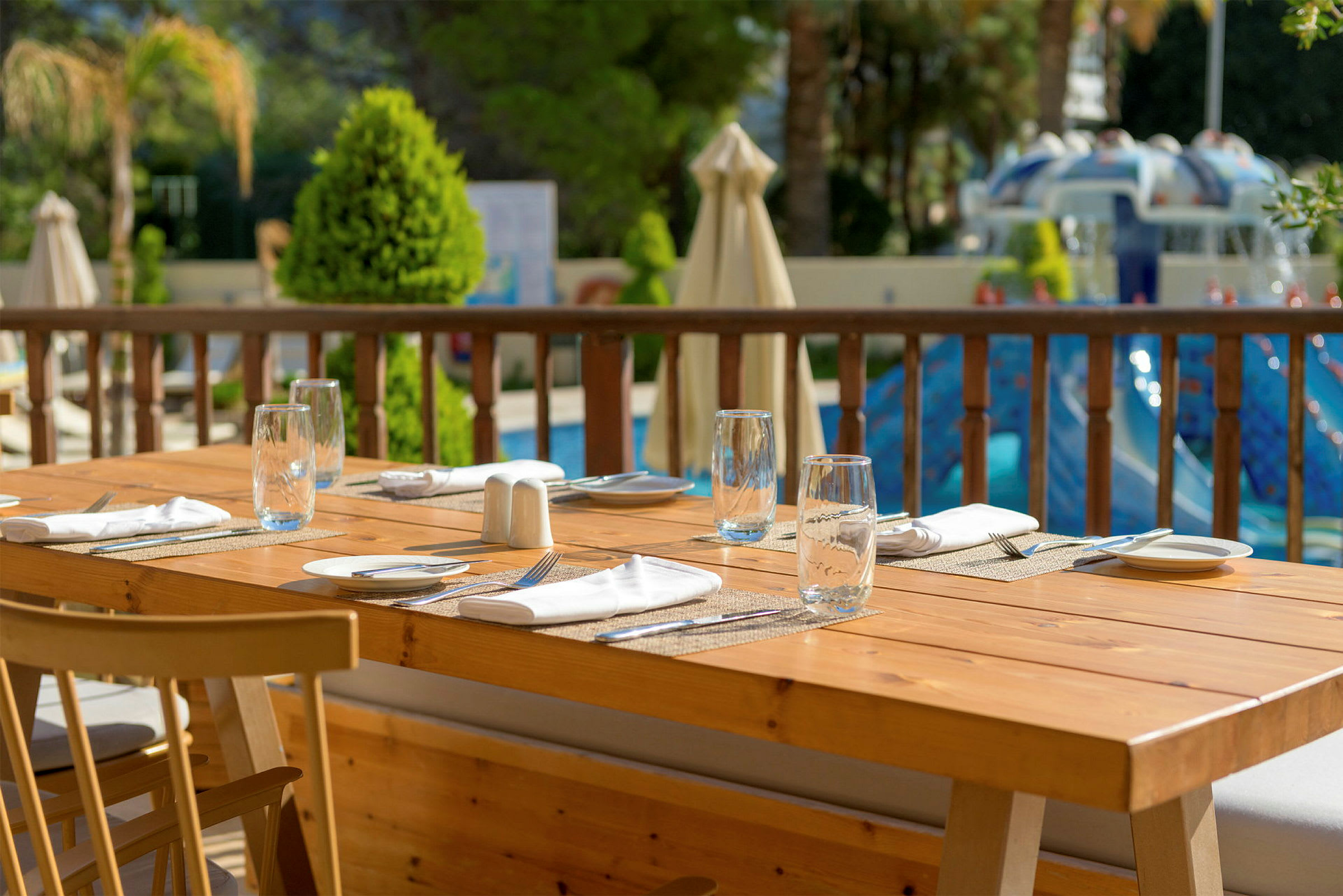 Ett dukat träbord med glas och bestick med utsikt över en pool och grönska. (AI-genererad text)