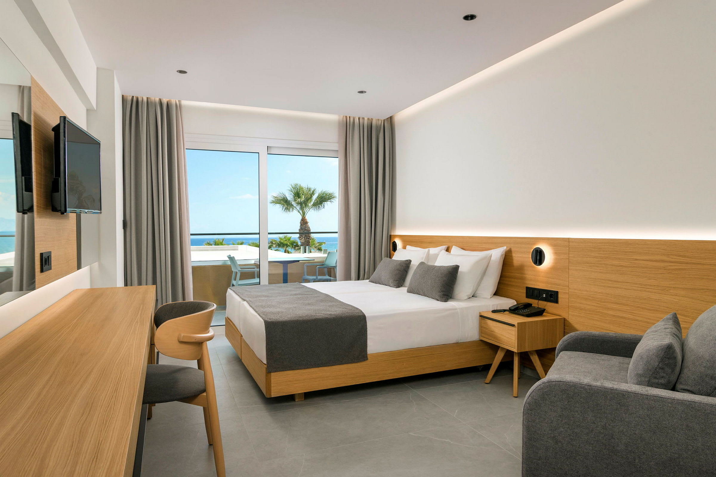 Hotellrum med dubbelsäng, grå inredning och utsikt mot havet. (AI-genererad text)
