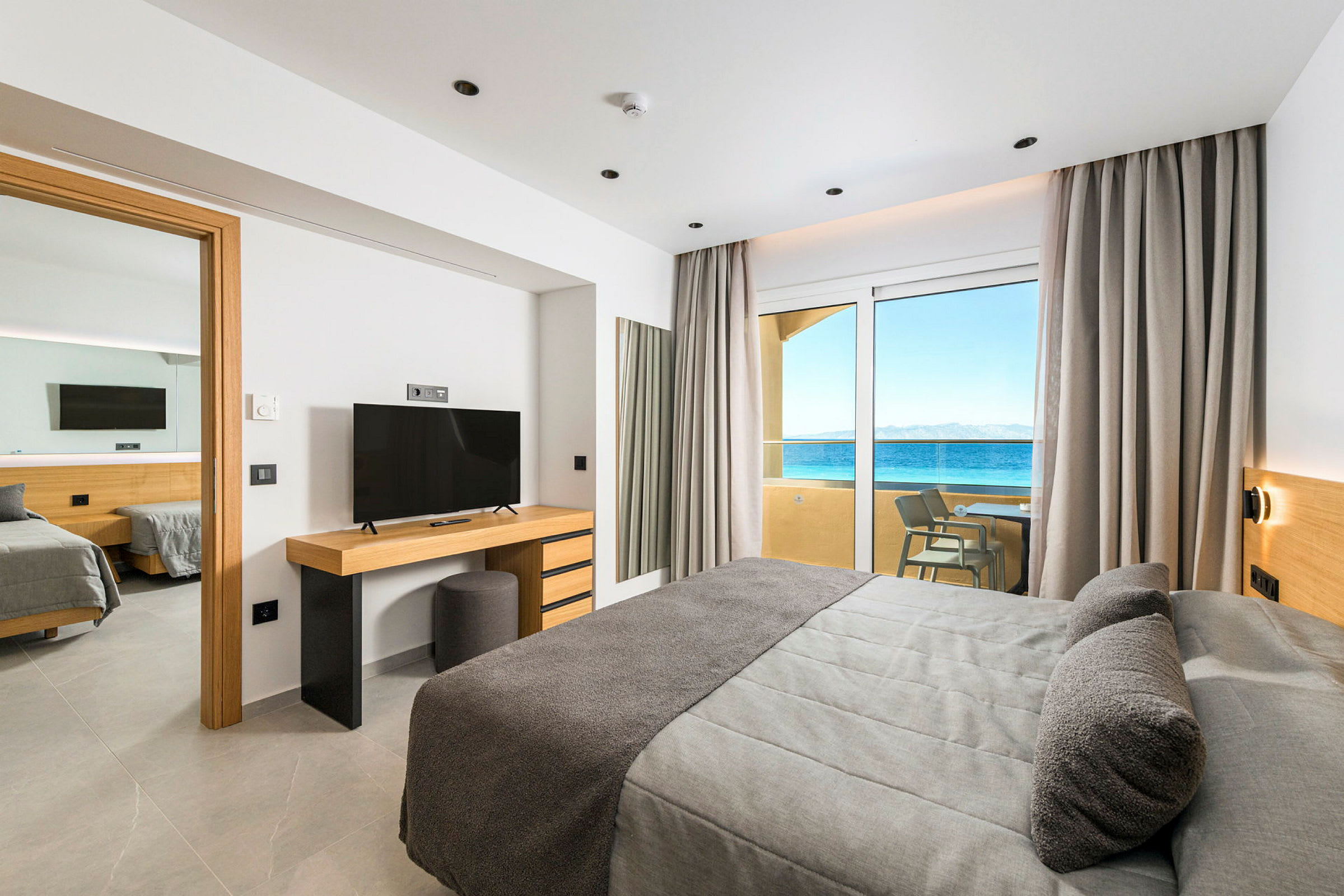 Hotellrum med modern inredning, havsutsikt genom glasdörrar och tillgång till balkong. (AI-genererad text)