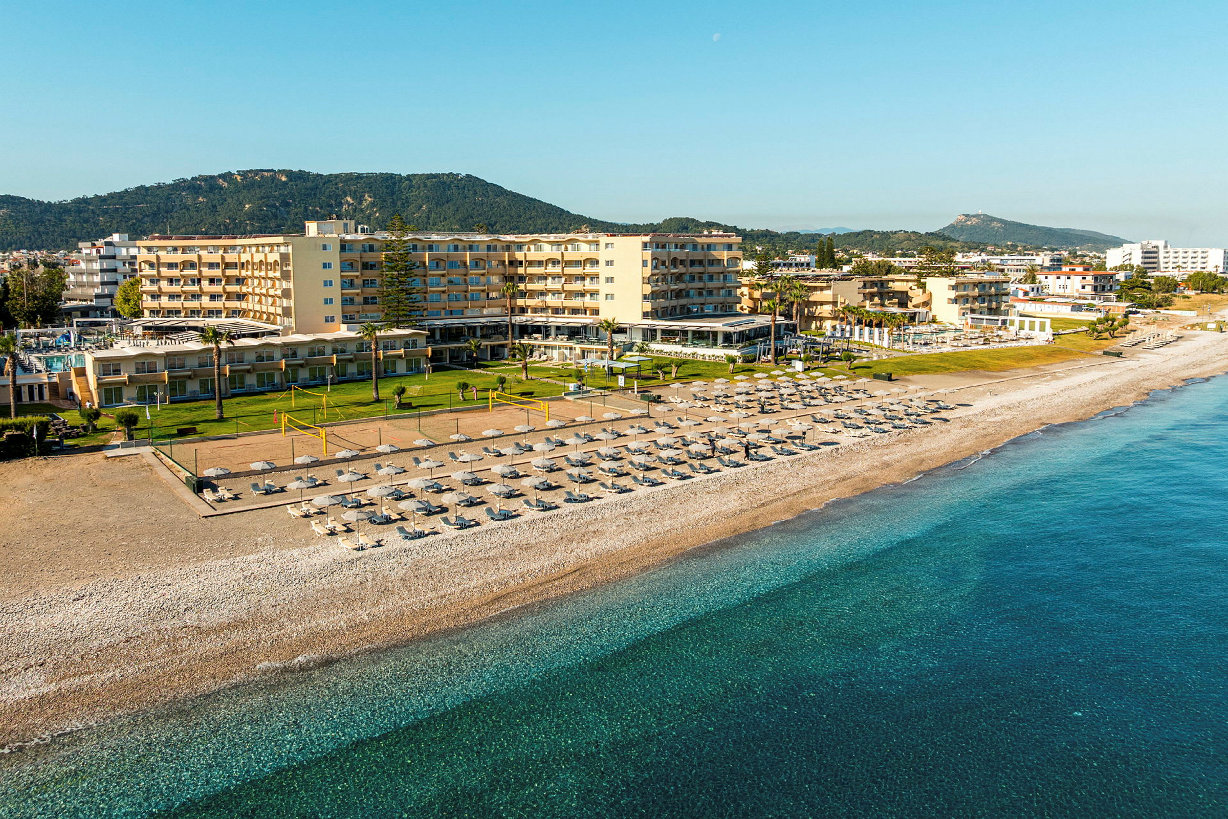 En strand med parasoller och solstolar framför ett hotellkomplex och grönska. (AI-genererad text)