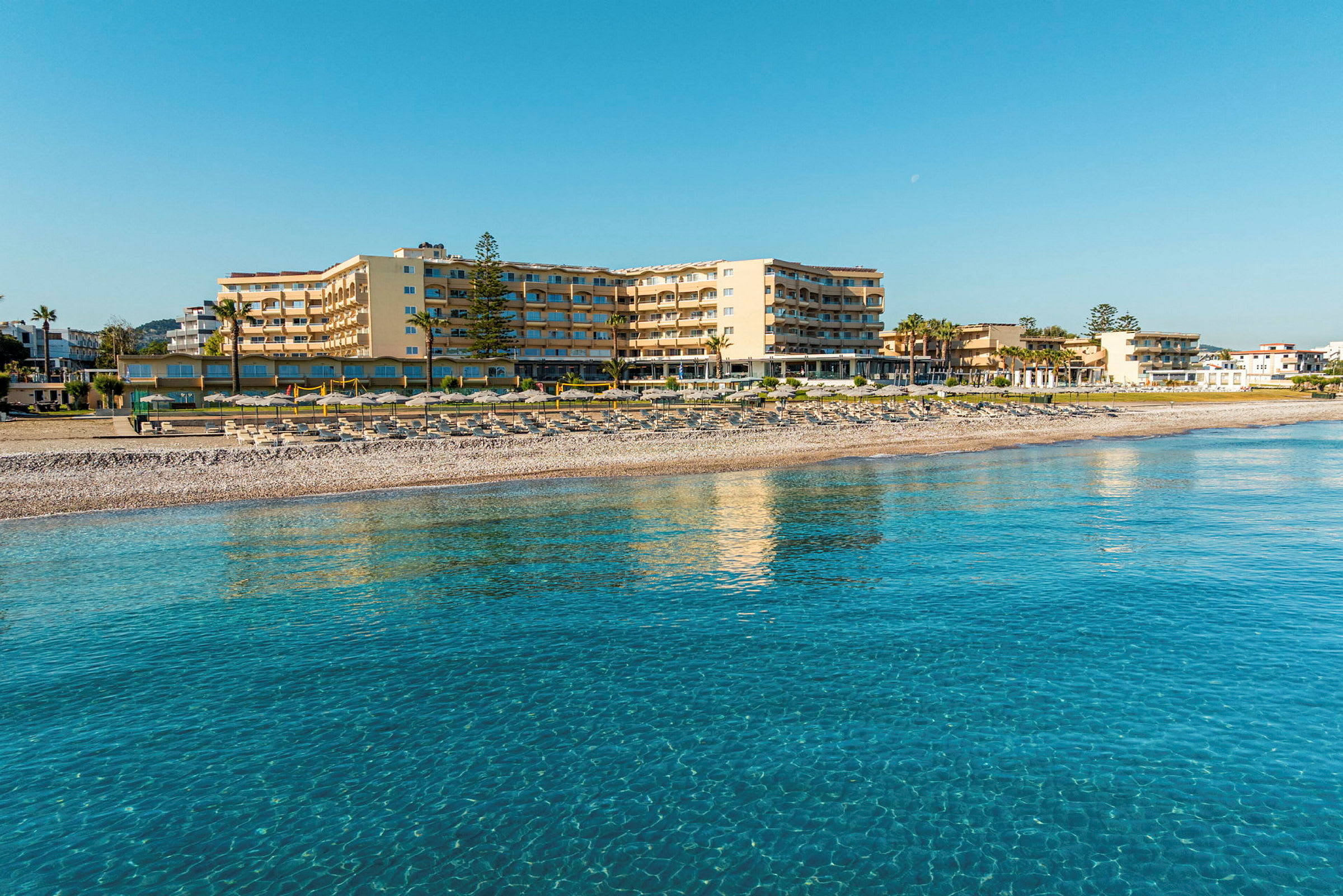Ett hotell vid stranden med klart blått vatten i förgrunden. (AI-genererad text)
