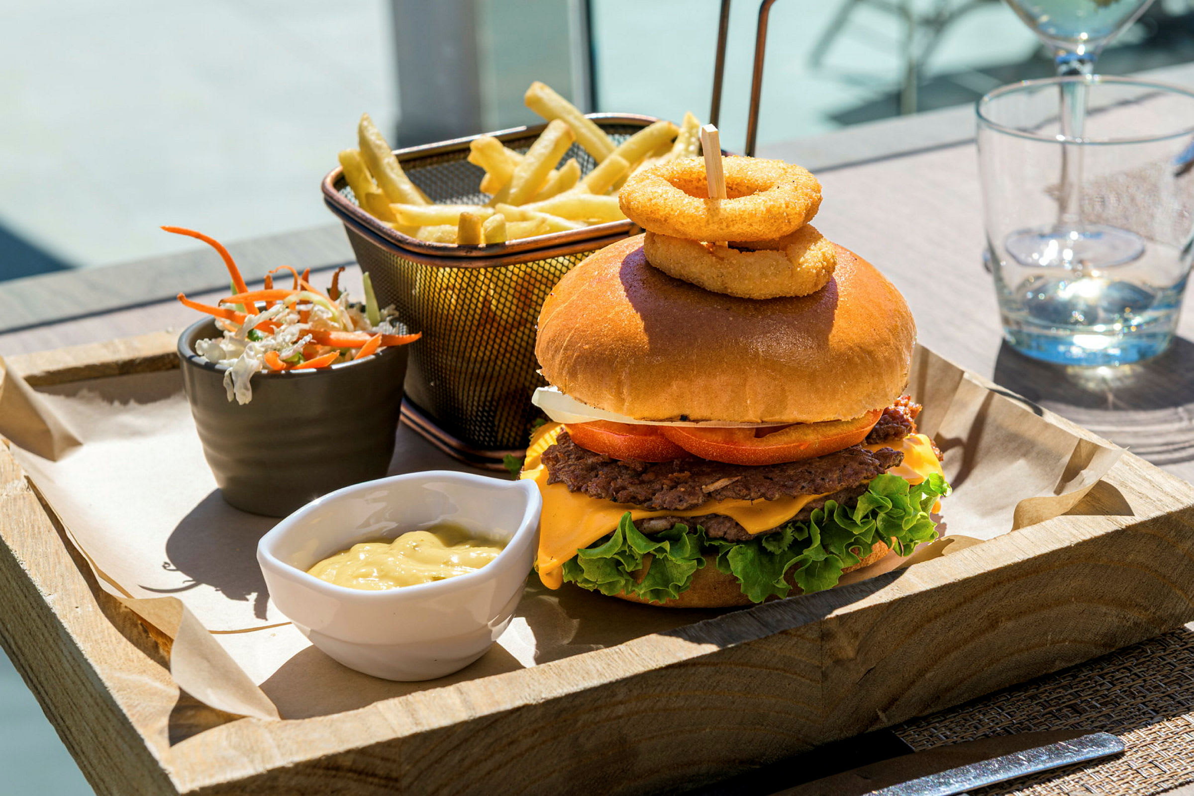 En måltid med hamburgare, pommes frites, salladsblandning och sås serveras på en träbricka. (AI-genererad text)