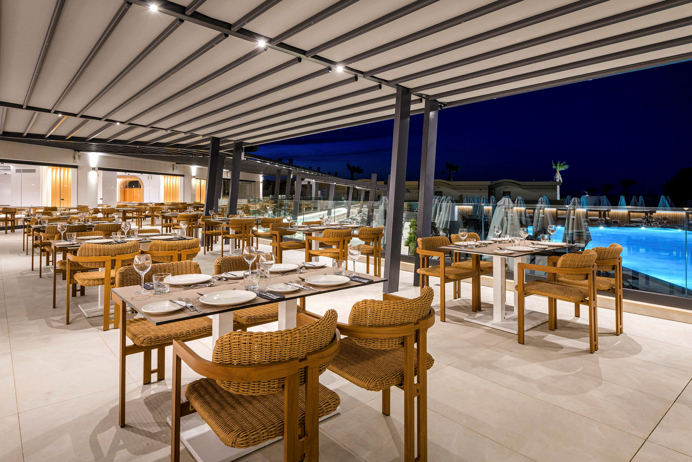 En restaurang med utomhus sittplatser, dukade bord och utsikt mot en upplyst pool. (AI-genererad text)