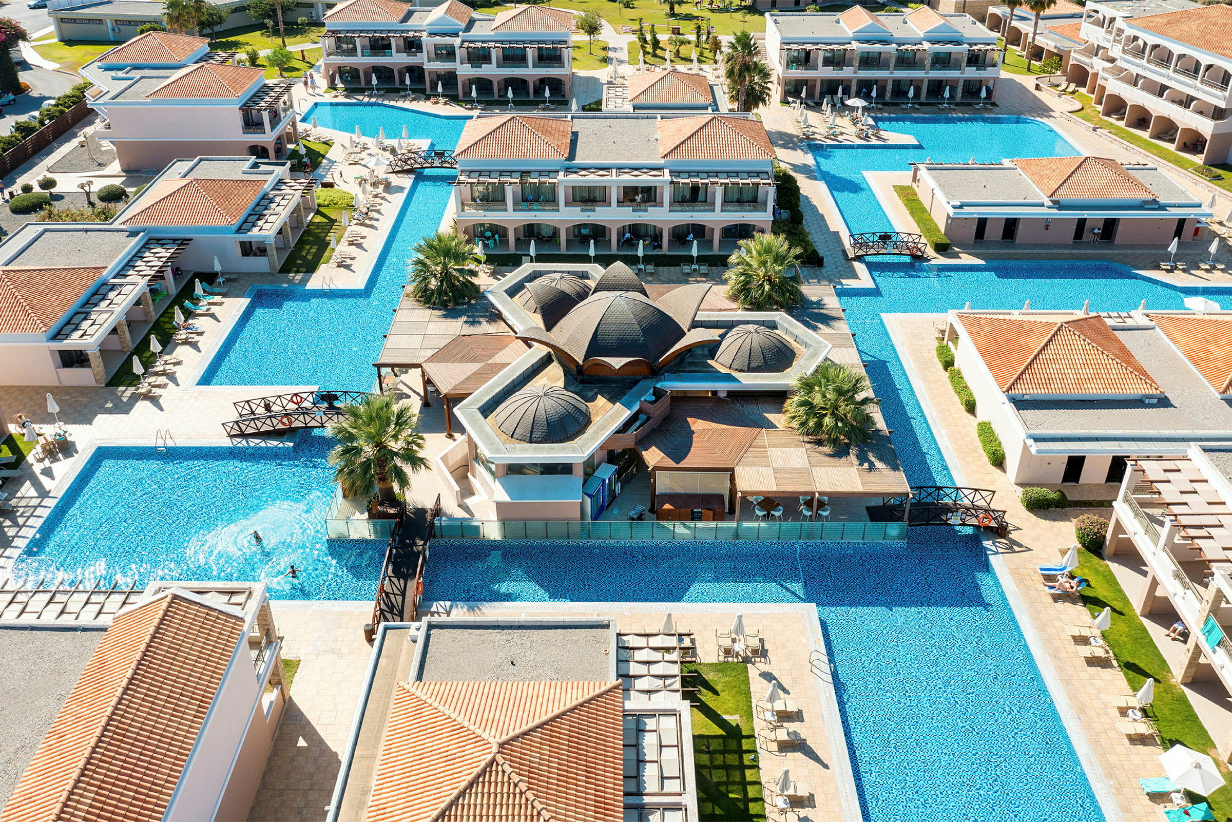 Flygbild över hotellområdet med omgivande pooler, byggnader och grönområden. (AI-genererad text)
