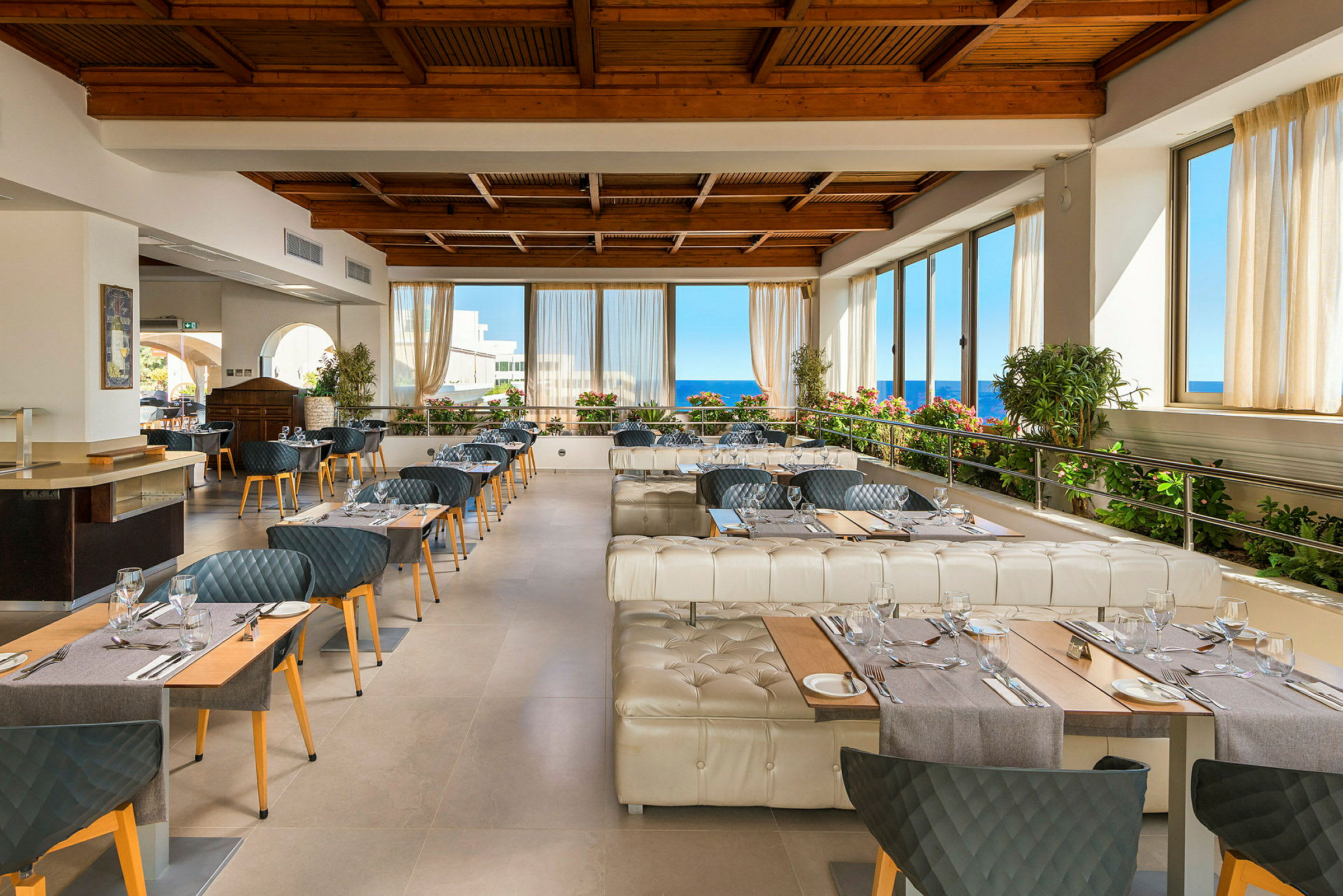 Restaurang med bord, stolar, och fönster med utsikt mot havet. (AI-genererad text)
