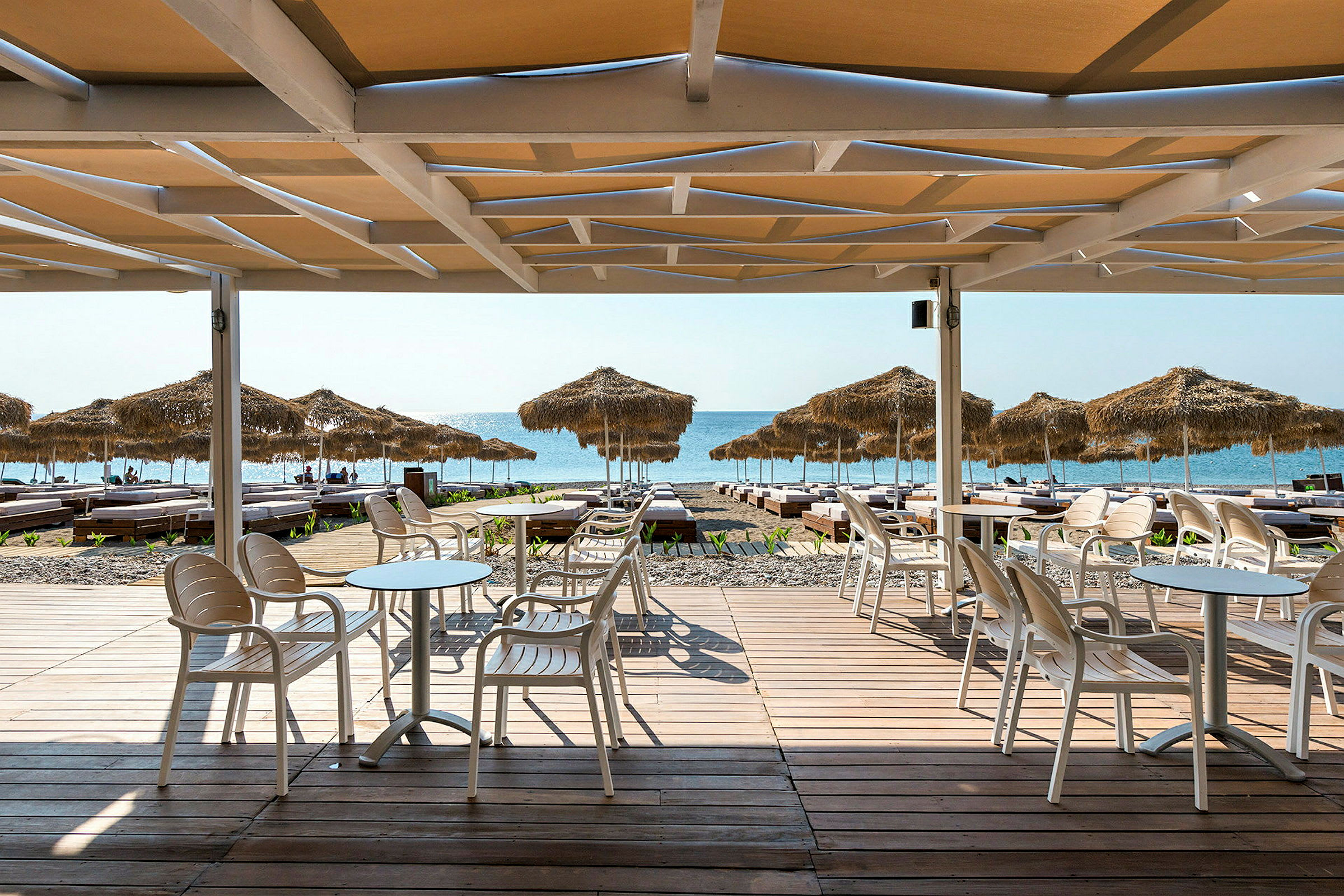 Strand med parasoller och solstolar, sett från ett trädeck vid en uteservering. (AI-genererad text)