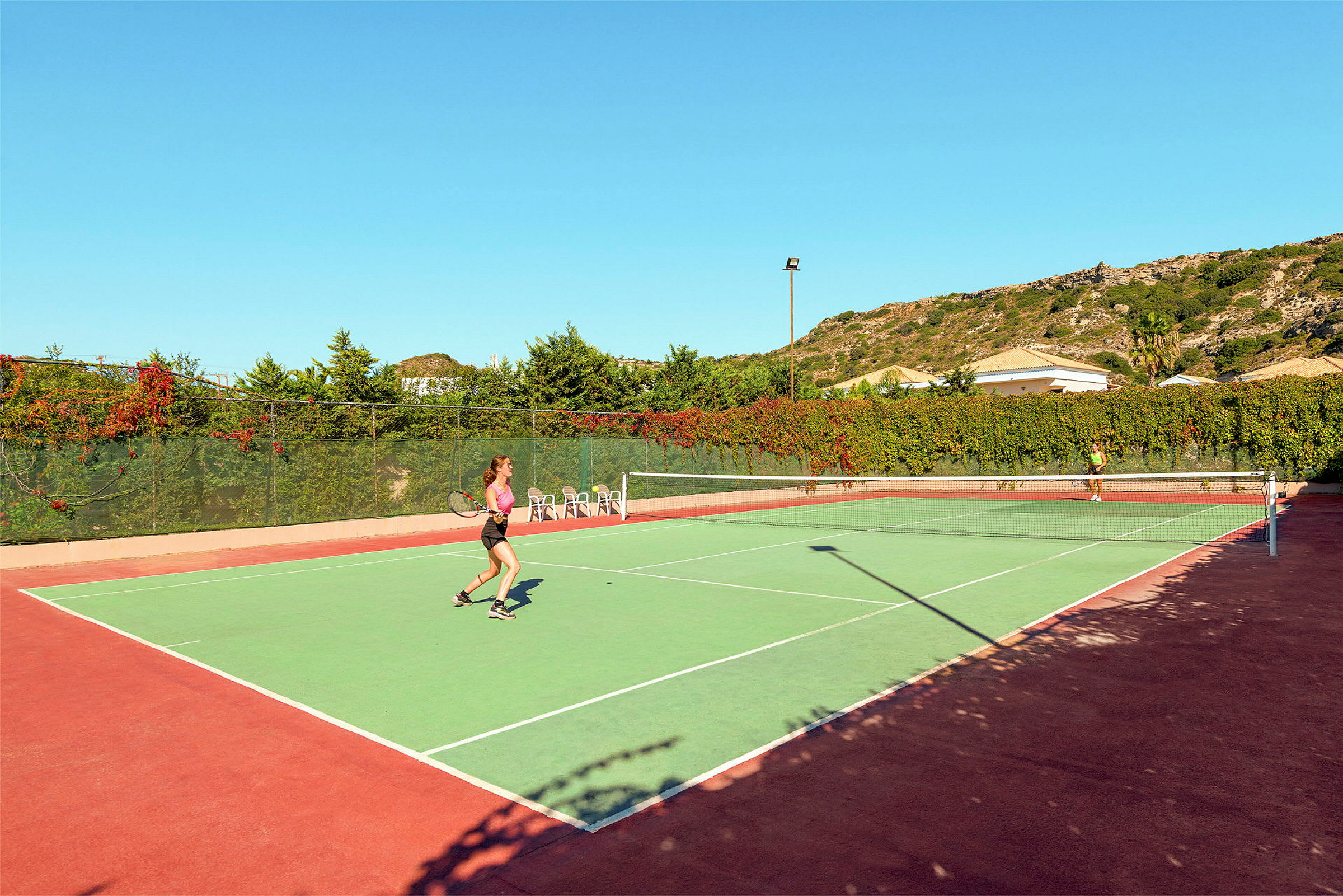 Två personer spelar tennis på en utomhusbana under klar himmel. (AI-genererad text)